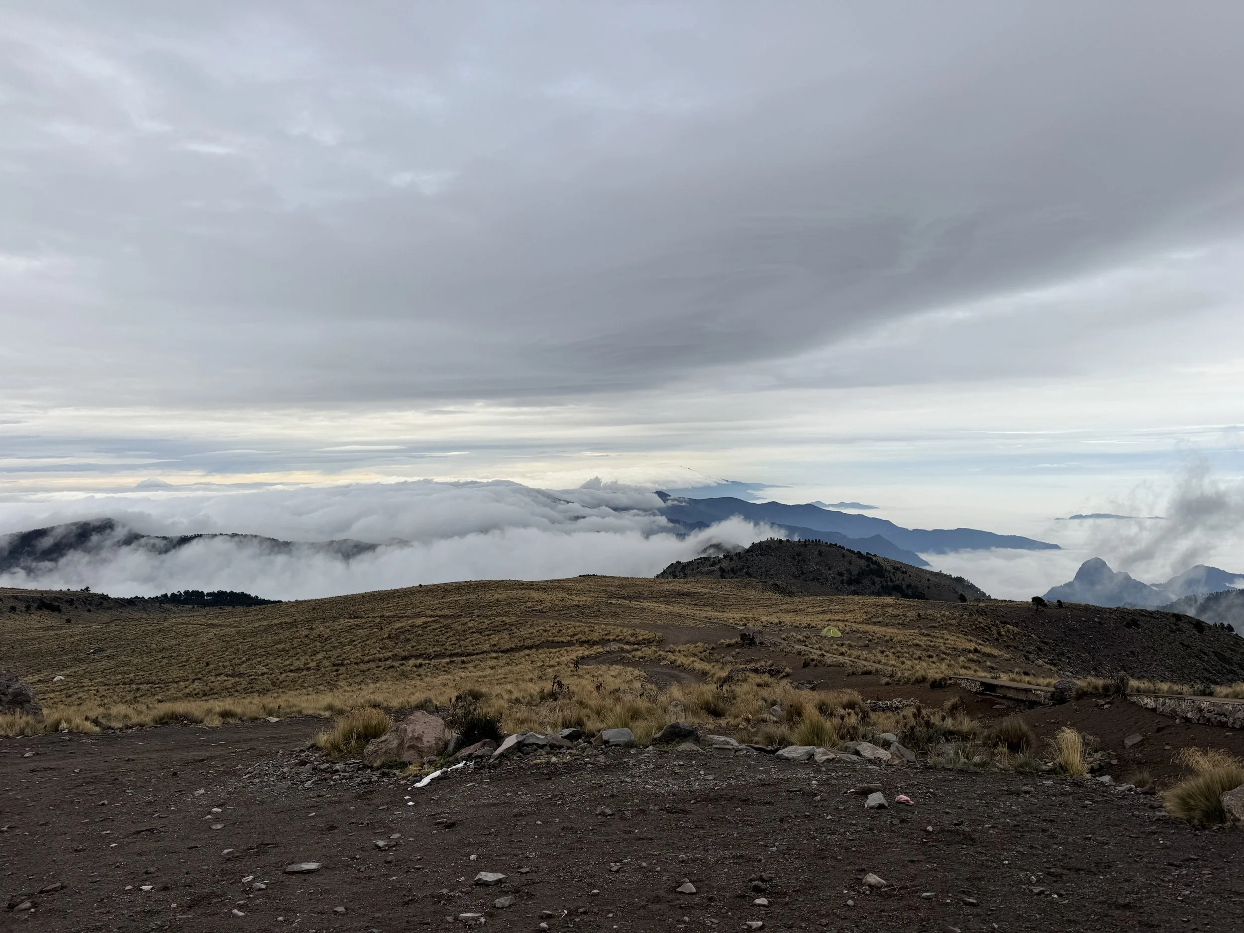 Mountain landscape with cloudy sky, distant mountains, and grassy terrain in foreground.