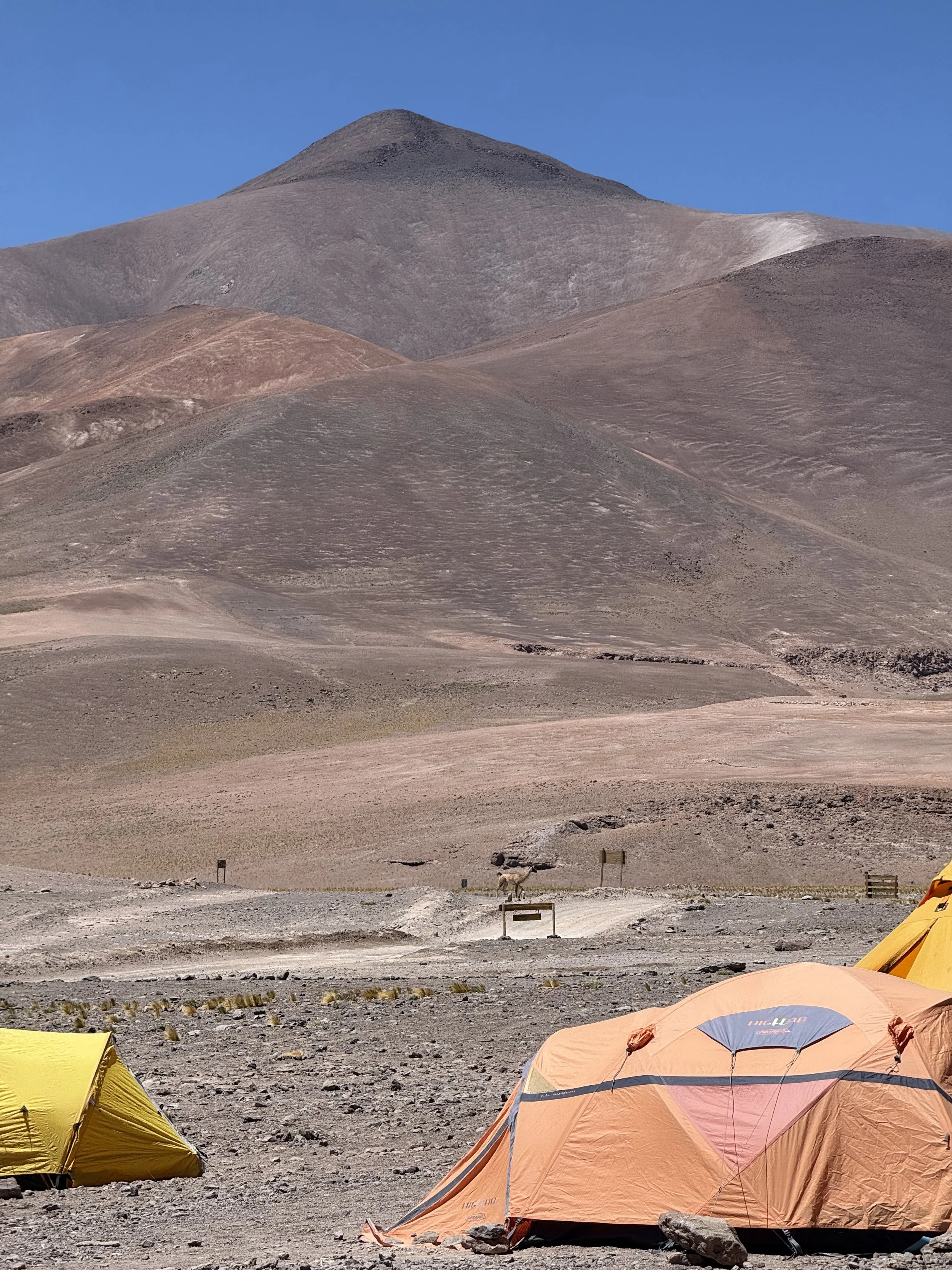 A desert landscape with mountain backdrop and a few tents in the foreground.