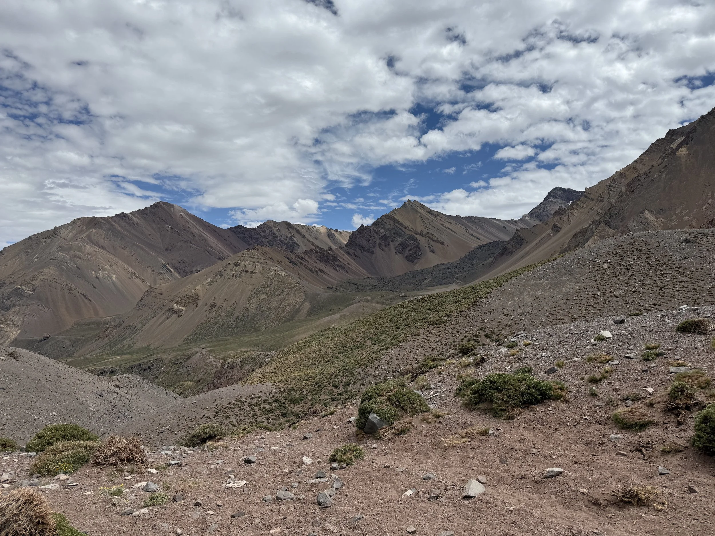 Mountain landscape with rocky terrain, sparse vegetation, and a partly cloudy sky.