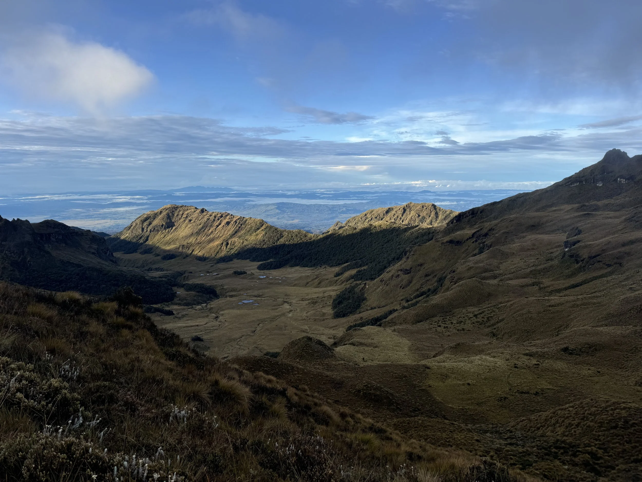 Scenic view of a mountainous landscape with rolling hills and valleys, under a partly cloudy sky with sunlight illuminating the terrain.