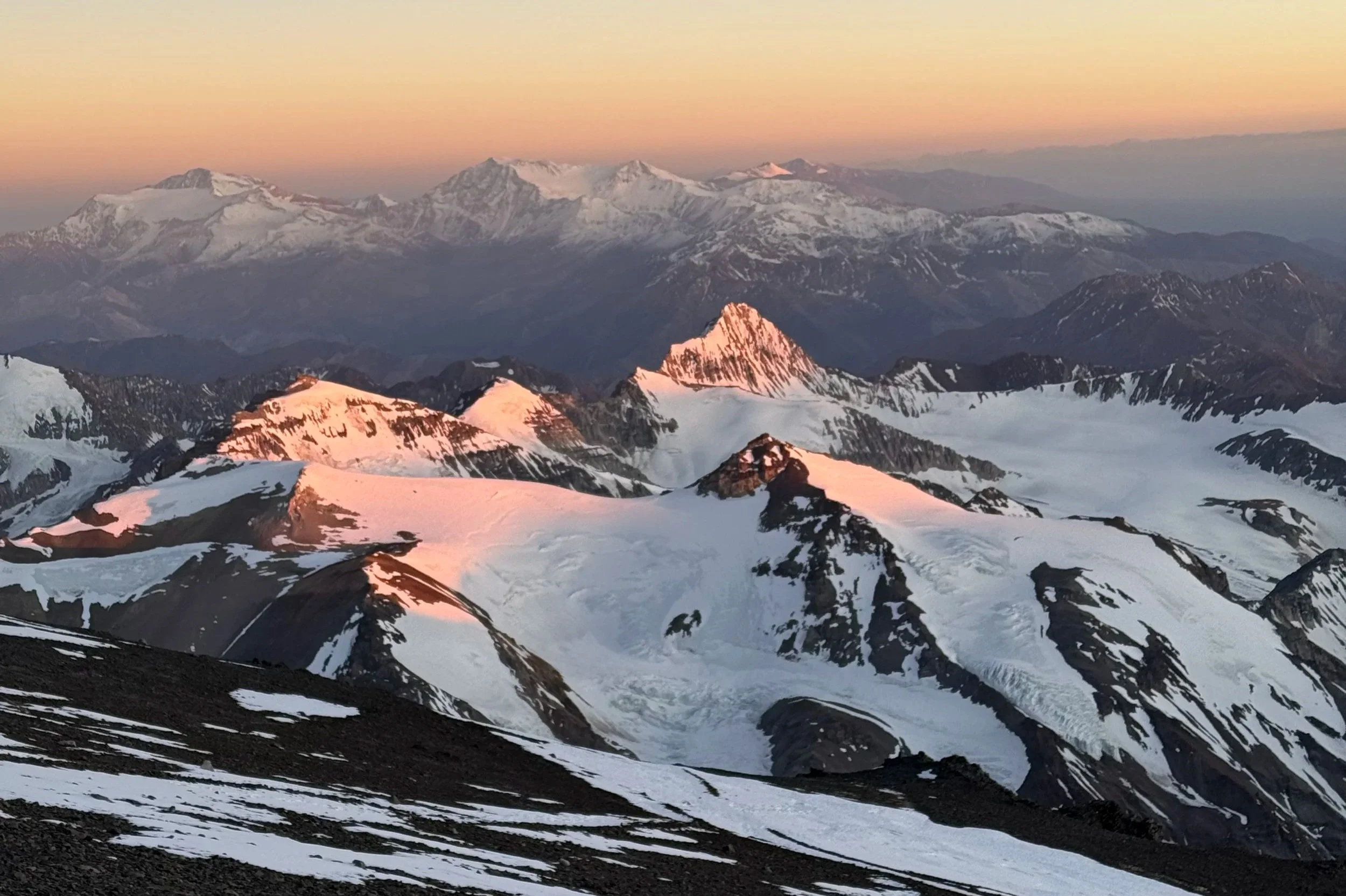 Snow-covered mountain peaks at sunset with a pink glow on the snow and a colorful sky in the background.