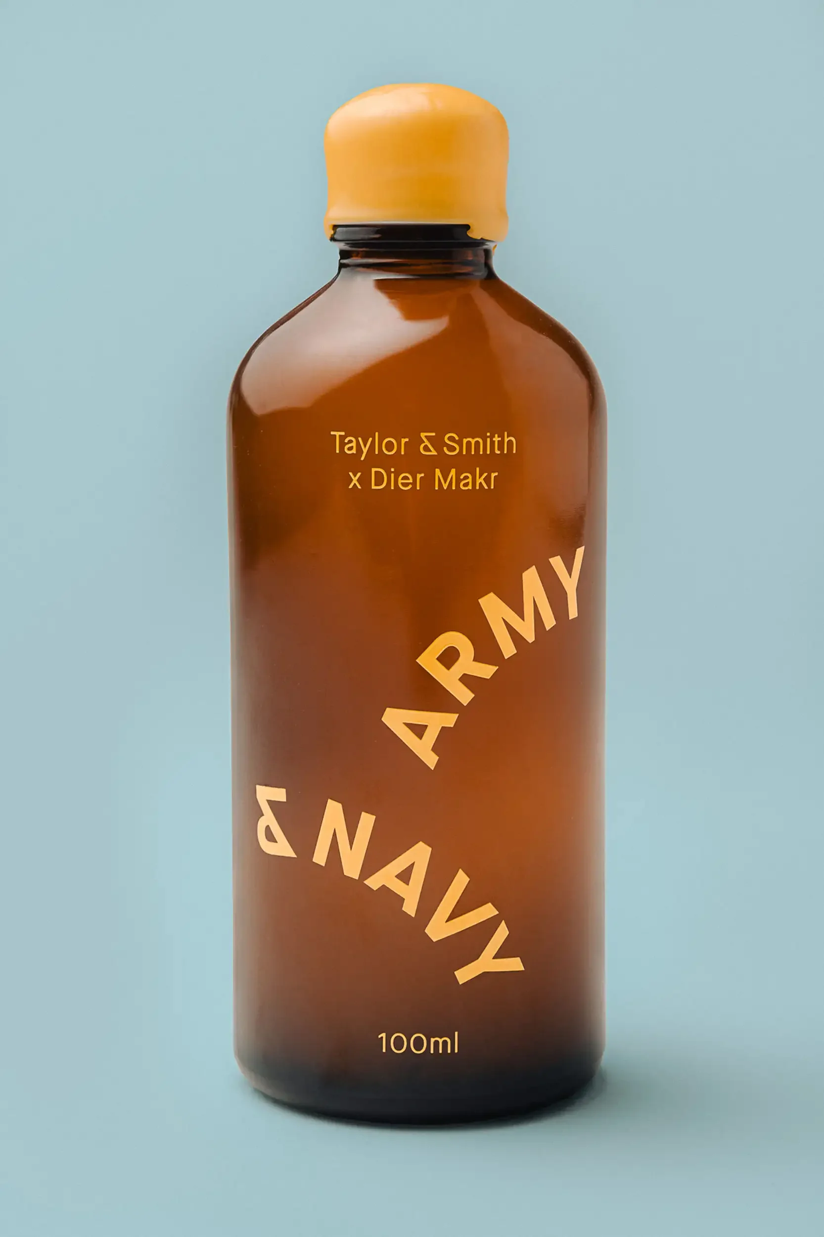 A brown glass bottle with a yellow cap. The label reads 'Taylor & Smith x Dier Makr' and features a diagonal text that says 'Navy ARMY' near the middle. The bottle contains 100ml of liquid.