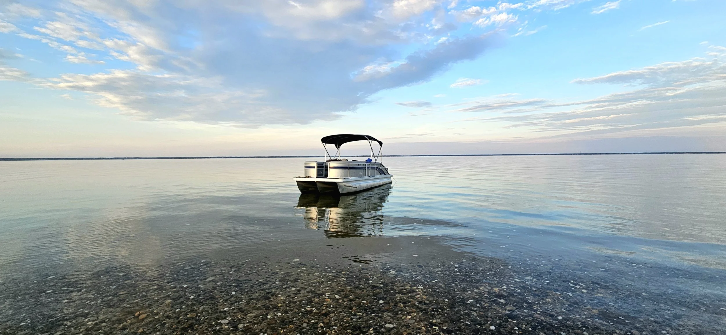 A small boat floating on calm water near the shoreline with a cloudy sky overhead.