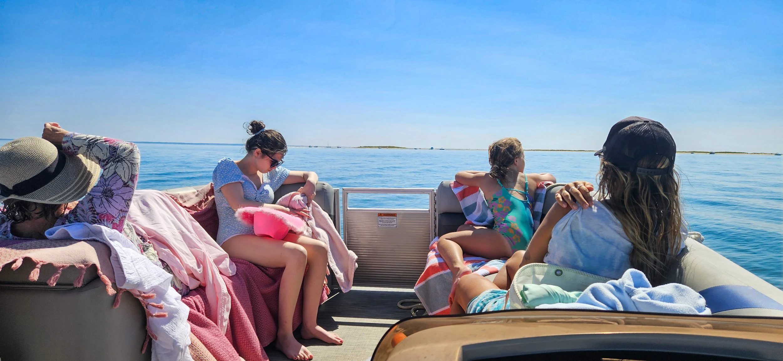 Four women and one girl relax on a boat, enjoying a sunny day on calm blue water.