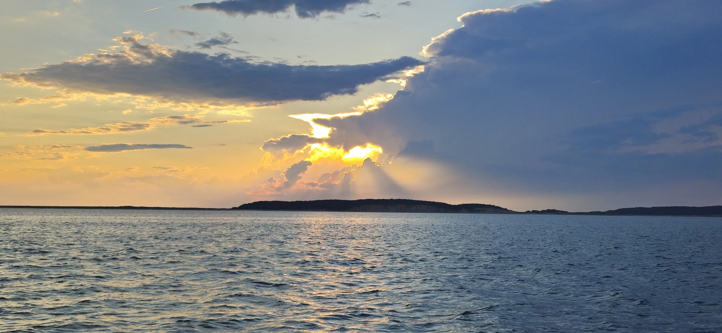 Sunset over a calm body of water with a distant island and partly cloudy sky