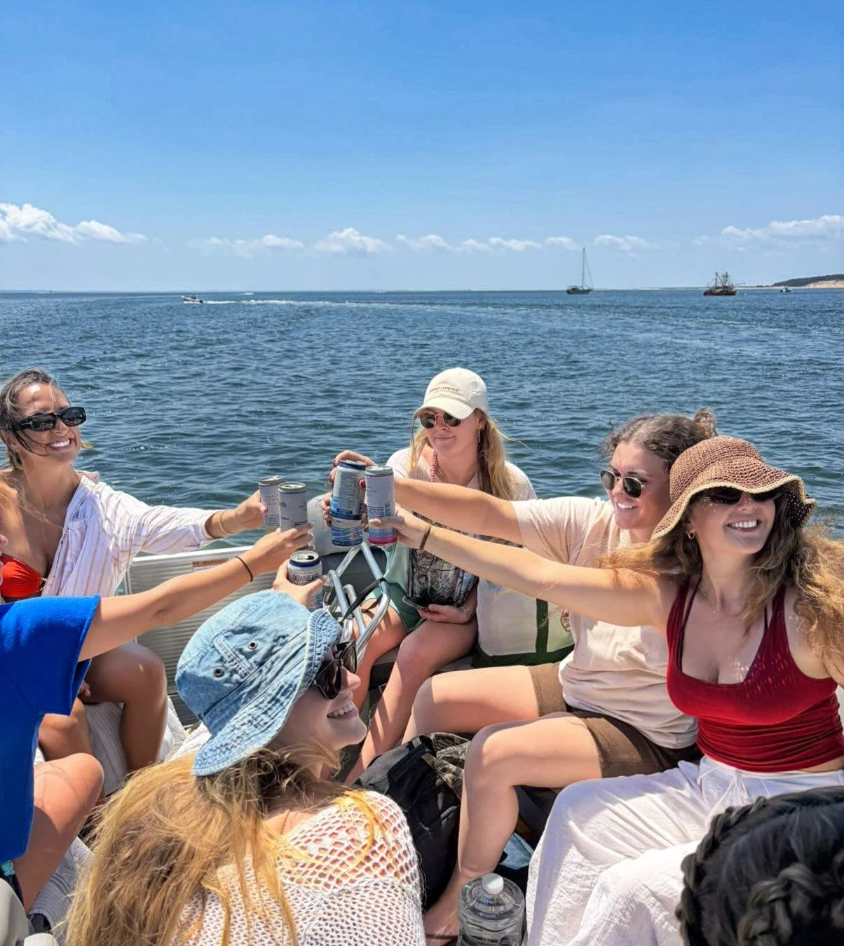 Group of women on a boat celebrating with drinks near the ocean on a sunny day.