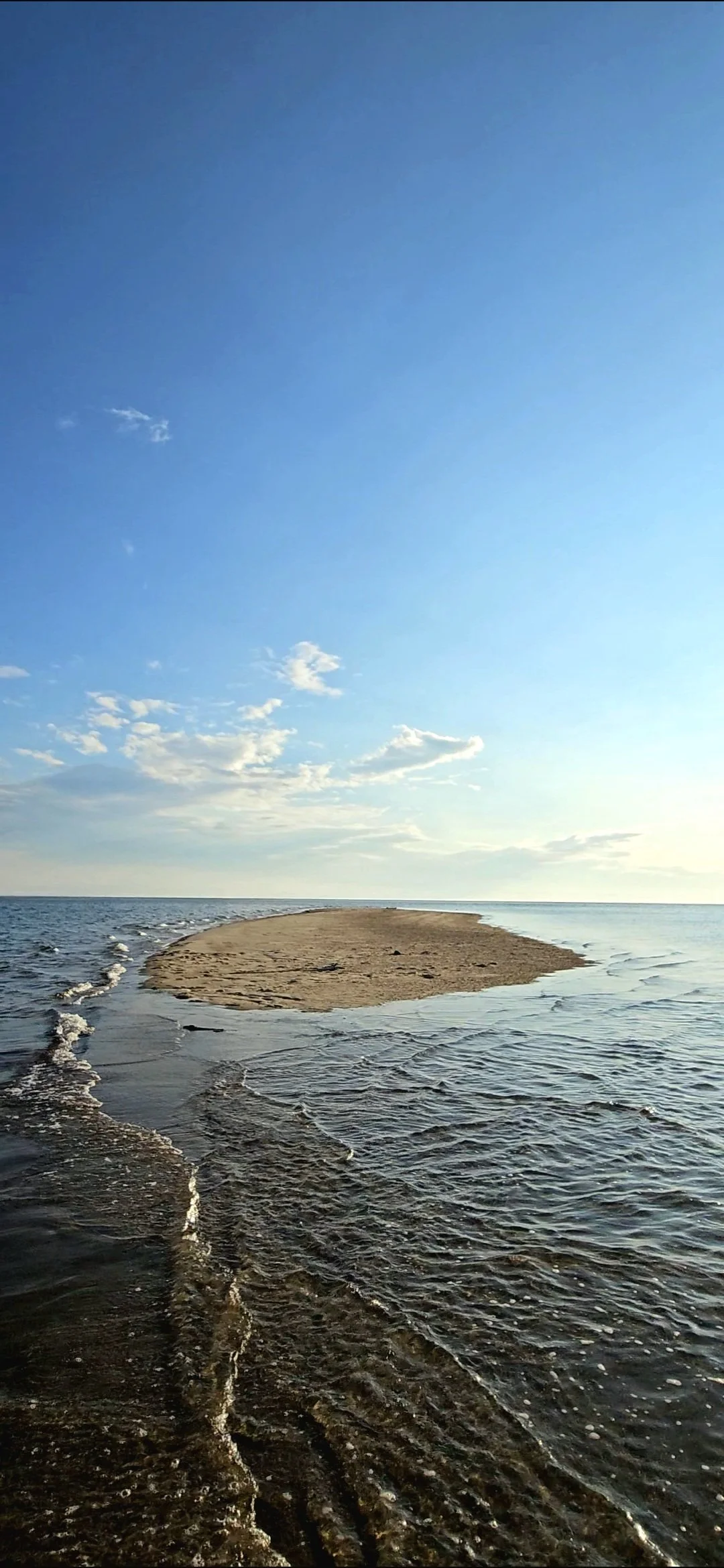 A sandy island or sandbar surrounded by water under a blue sky with some clouds.