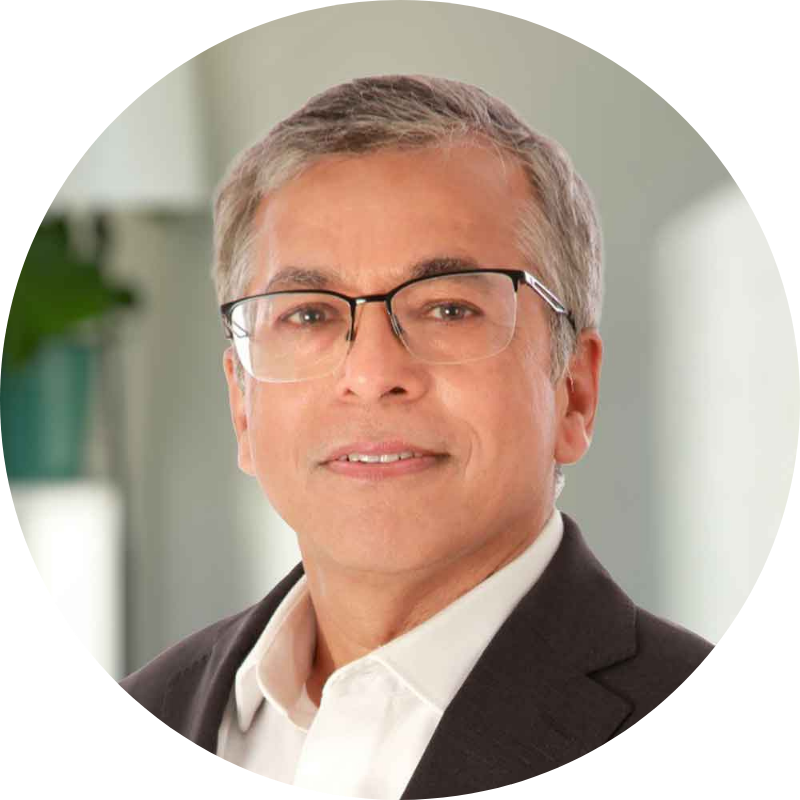 A middle-aged man with grey hair and glasses in a white shirt and black suit jacket softly smiling.