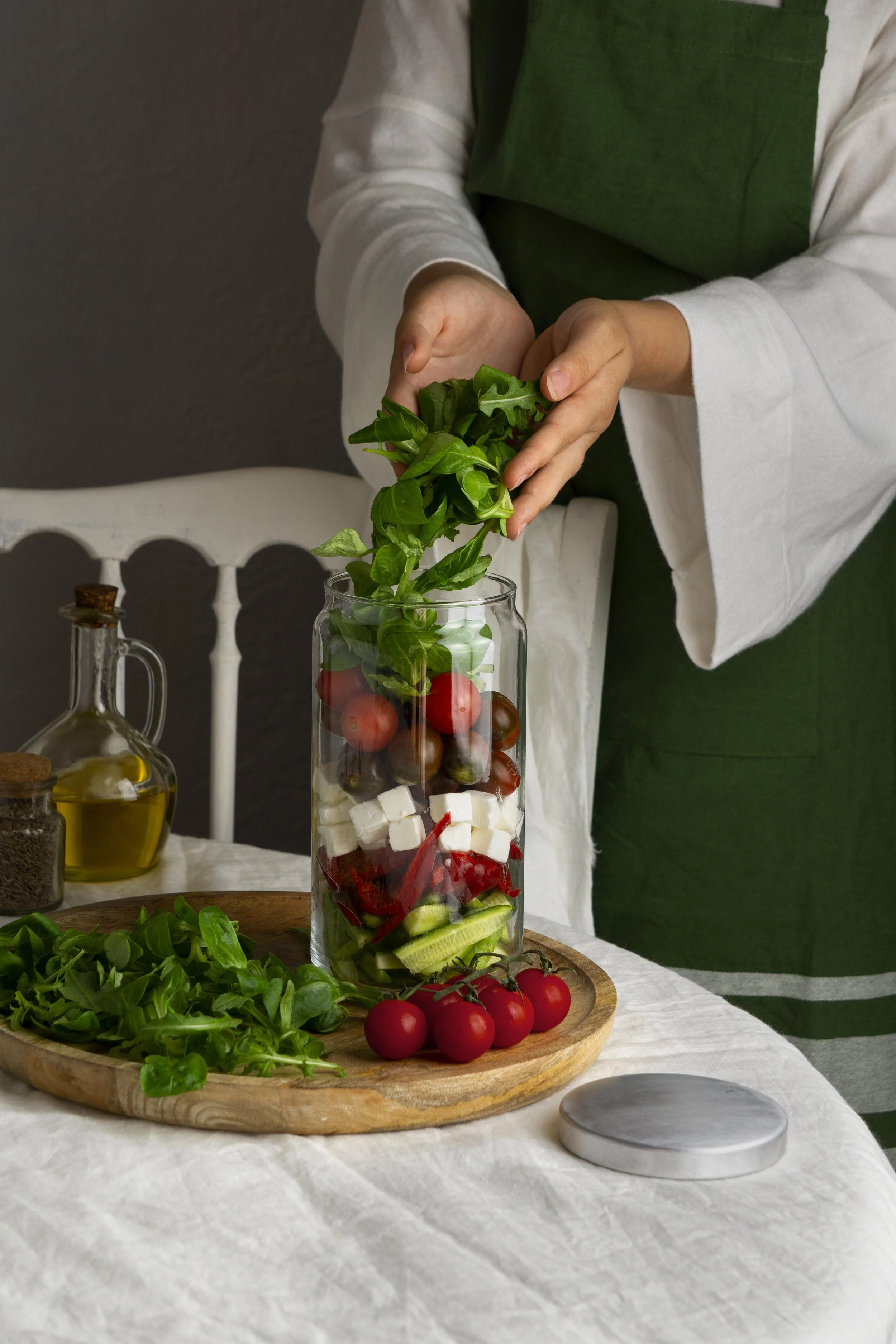 Photo d'une femme en train de rajouter de la salade dans un bol avec tomates crus, feta, concombre (tout est cru)