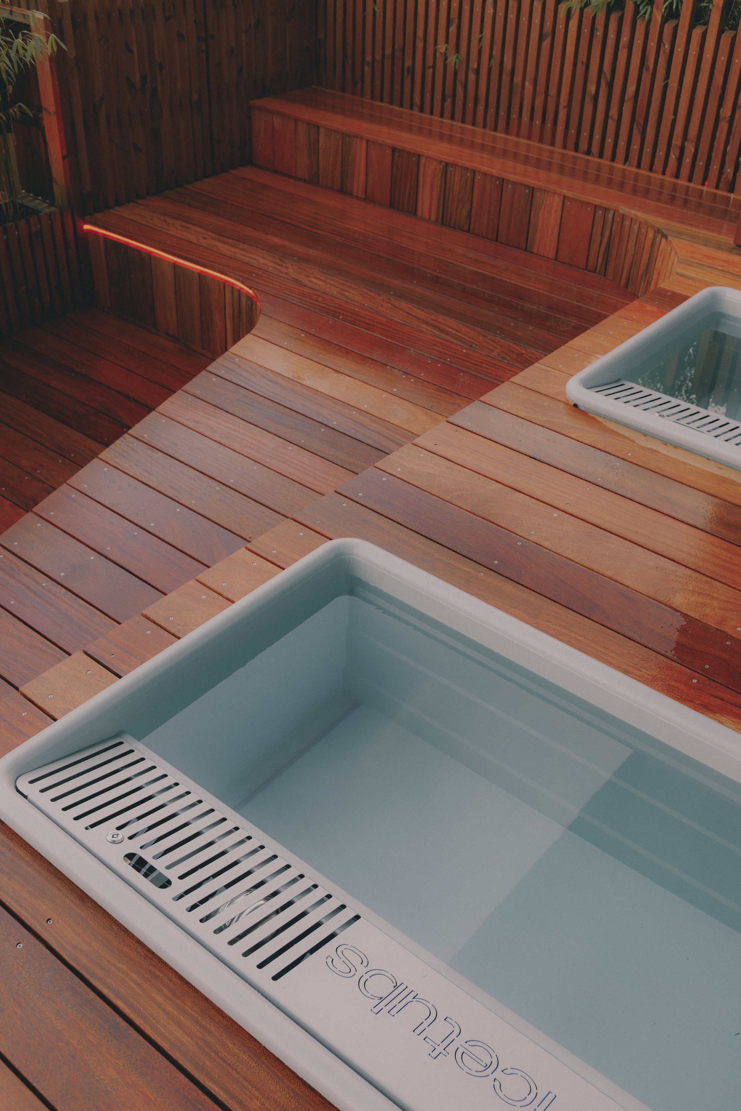 Wooden hot tub with built-in seating and two rectangular pools filled with water, set on a wooden deck surrounded by a wooden fence. Holm8 Icetub pro