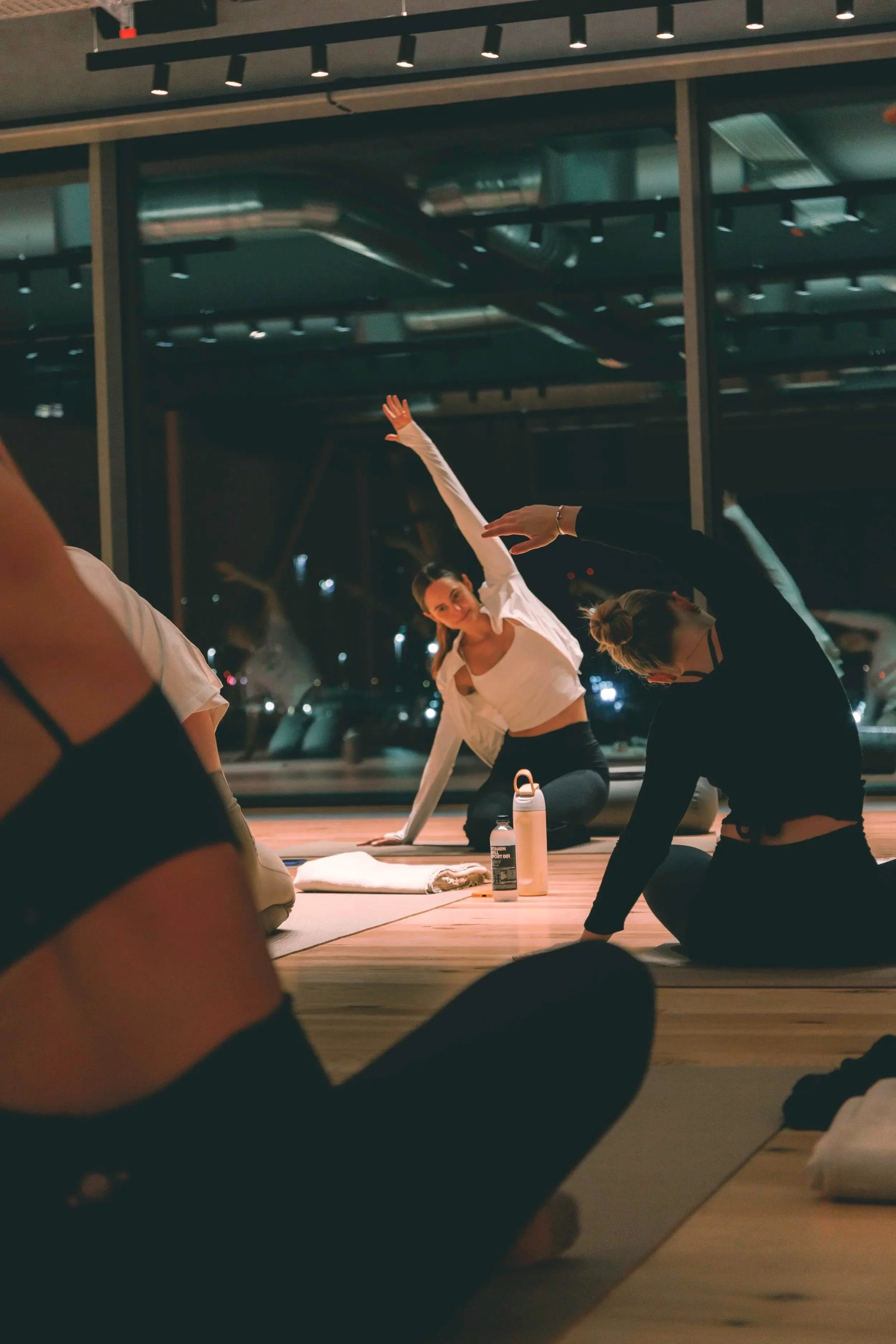 People doing yoga in a studio at night with large windows, practicing stretches or poses on mats. Holm8