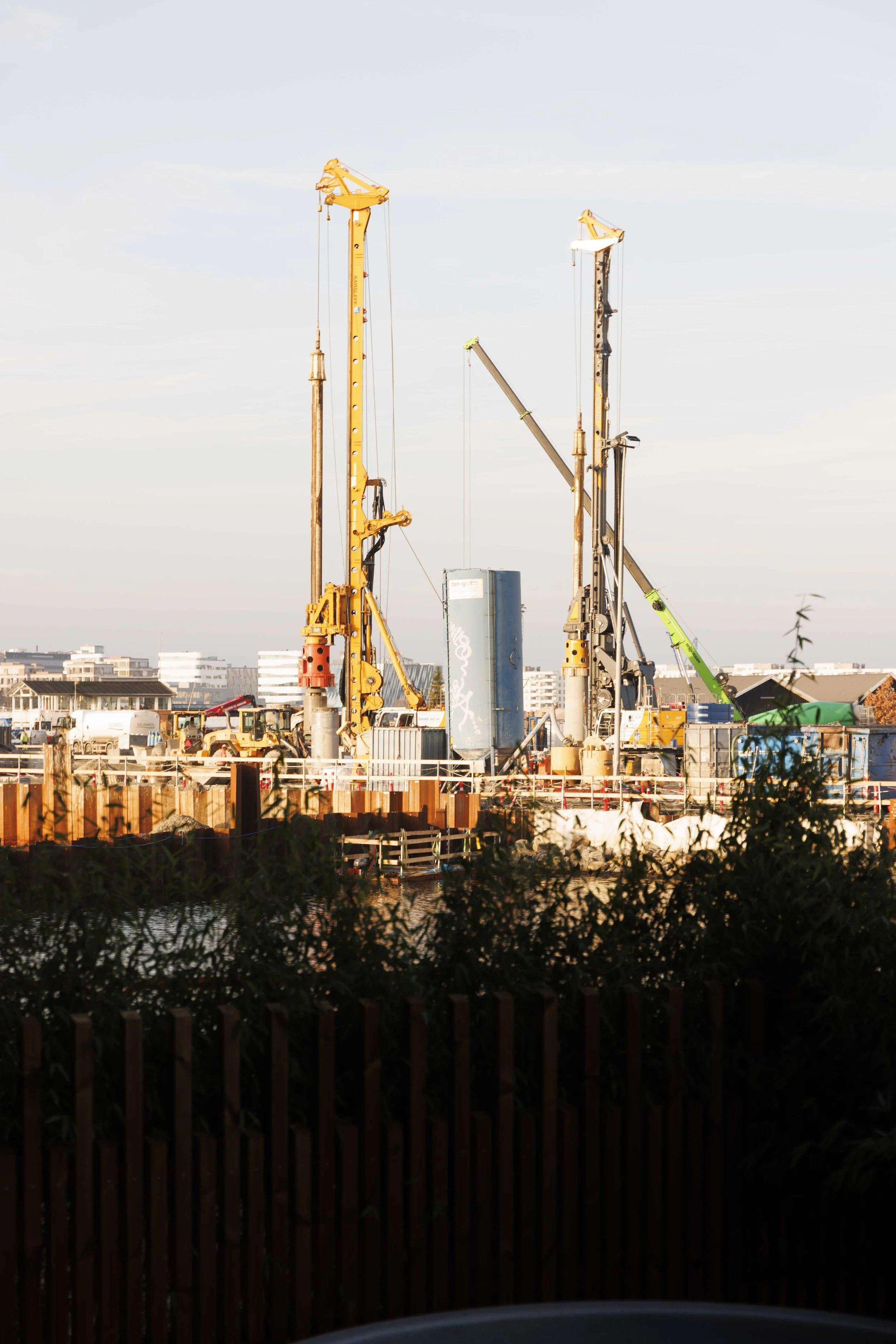Construction site with multiple large drilling machines and equipment, set against a cityscape background.