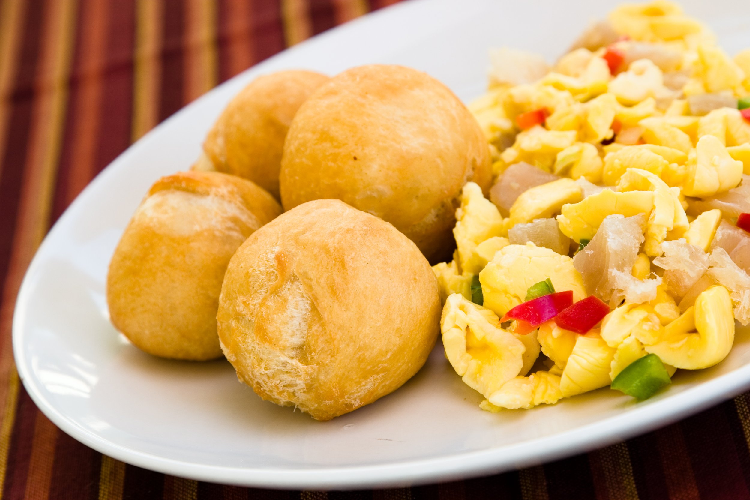 Ackee and saltfish with vegetables on a white plate, with fried dumplings.