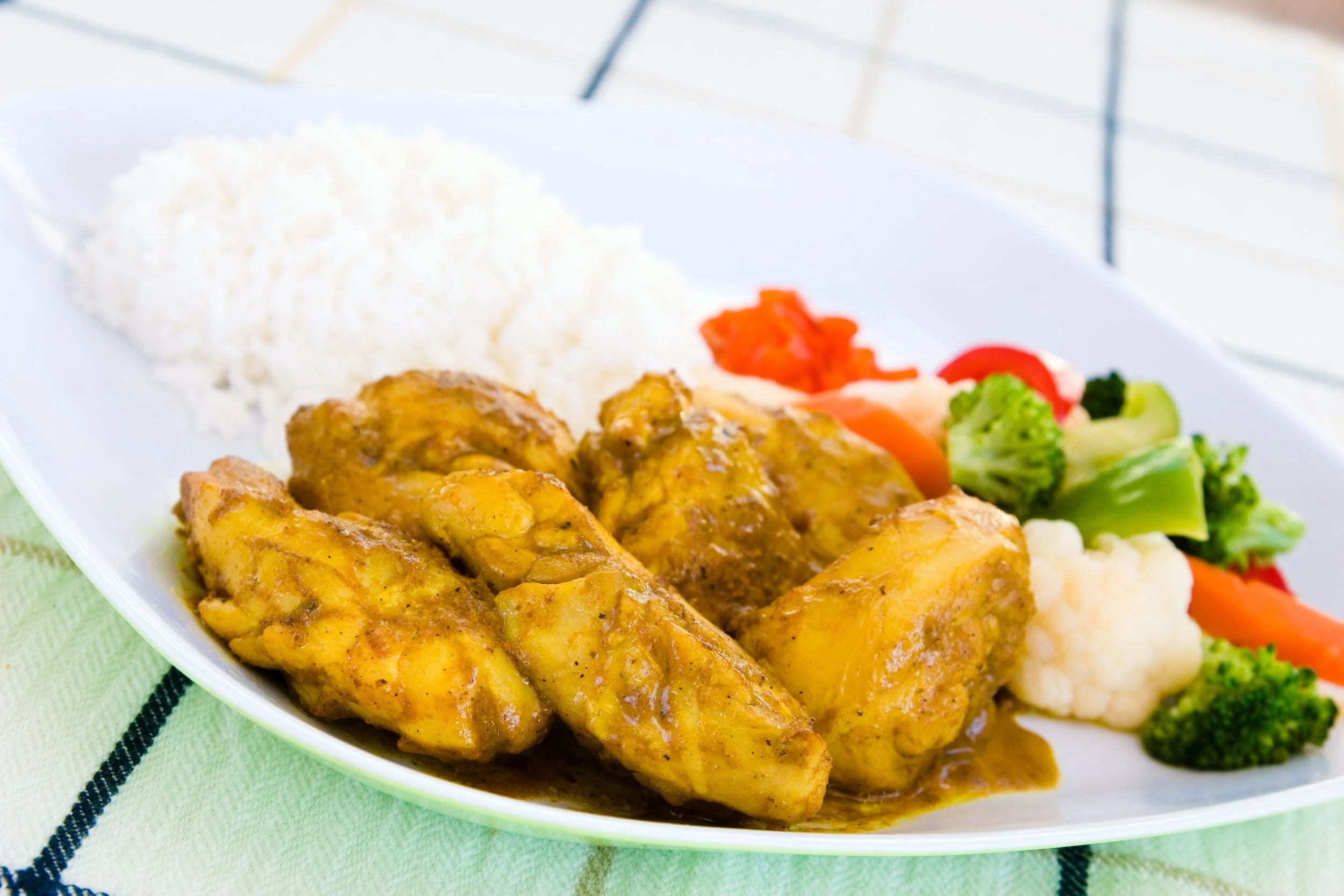 Plate with white rice, cooked curry chicken, and mixed vegetables including broccoli, cauliflower, carrots, and tomatoes.