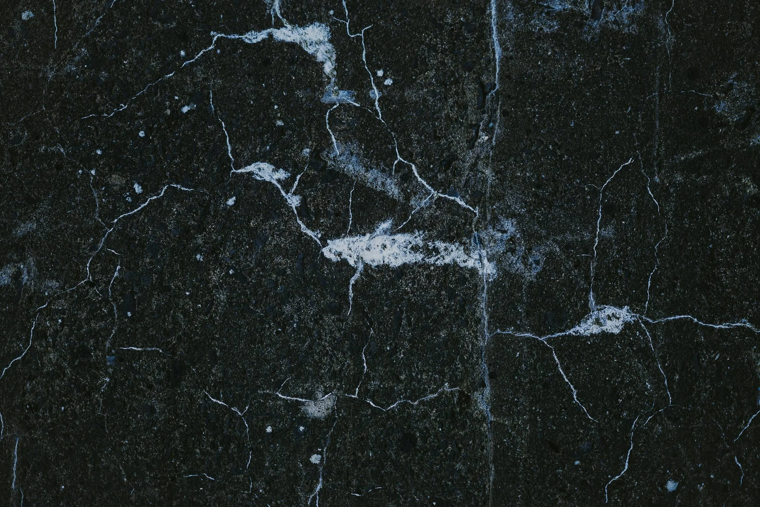 Surface en béton noir avec des fissures blanches.