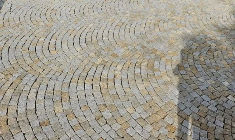 Un pavé de pierre formant un motif circulaire avec un mélange de couleurs beige et gris, et la silhouette d'une personne se reflétant sur la surface.