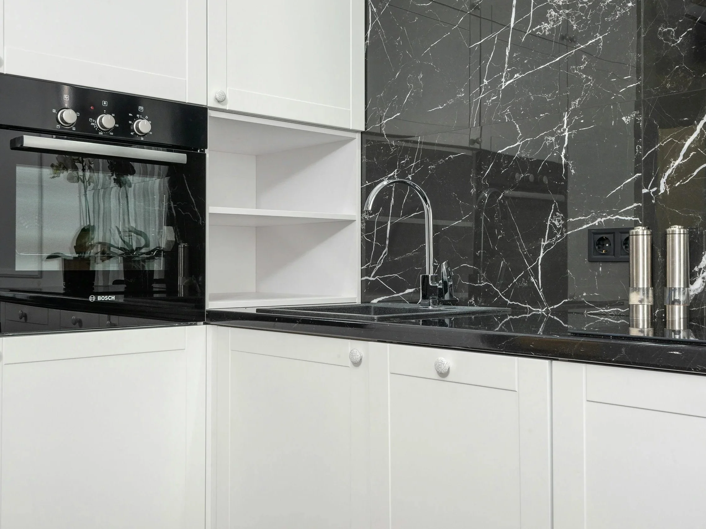 Cuisine moderne avec comptoir en marbre noir, évier en acier inoxydable, four à micro-ondes intégré, et dosseret en marbre noir veiné blanc. Deux moulins à poivre ou sel en acier inoxydable sont placés sur le comptoir.