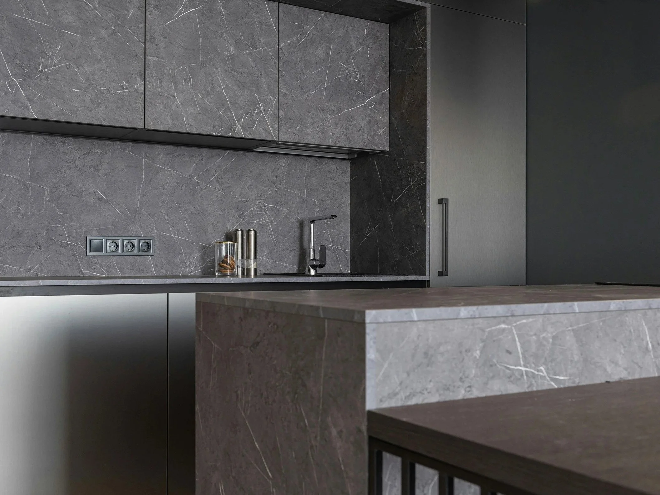 Cuisine moderne avec plans en marbre gris, armoires grises, évier en métal, et prises électriques intégrées.