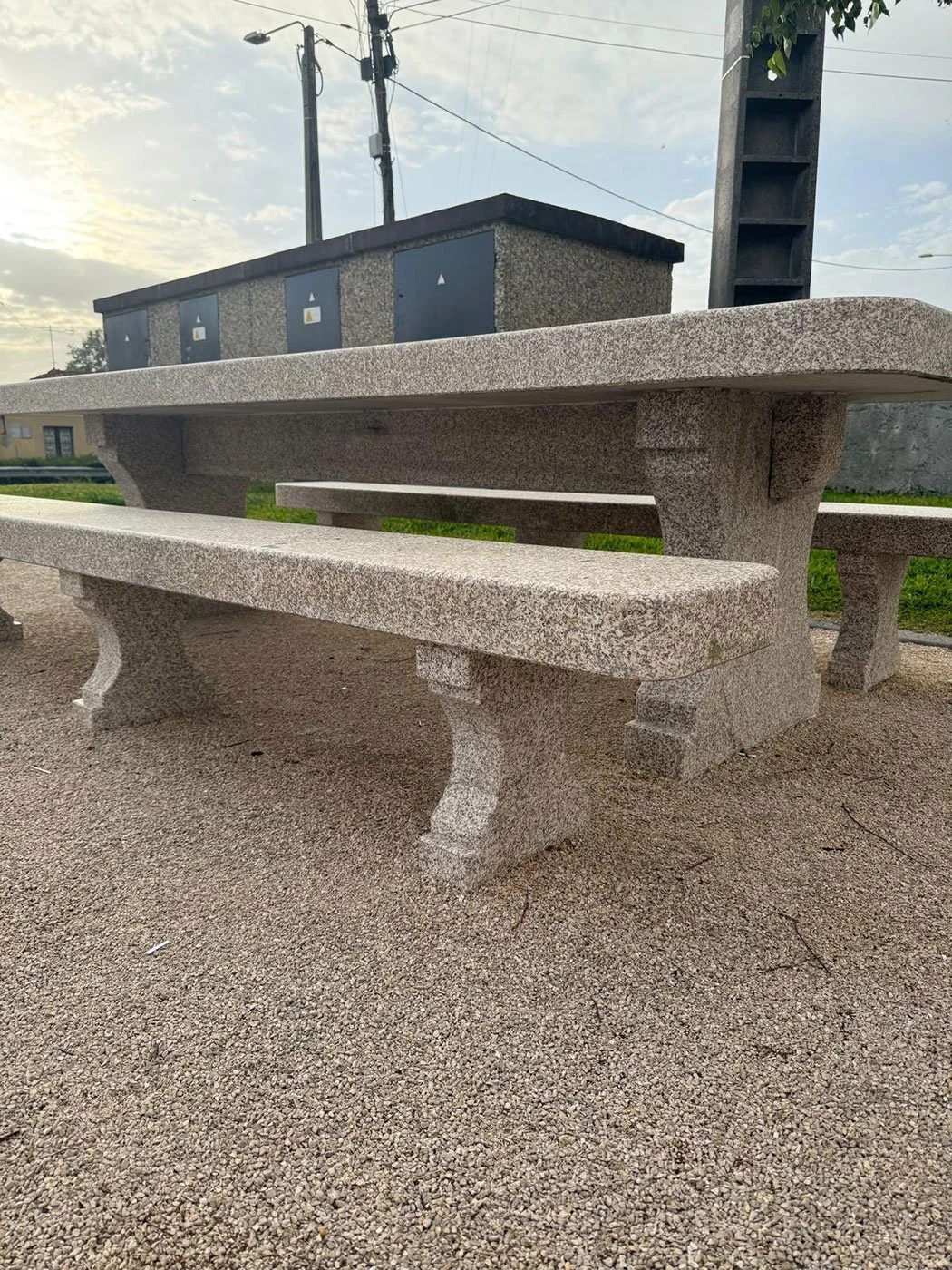Banc en pierre dans un parc en plein air, avec un ciel nuageux et des installations électriques en arrière-plan.