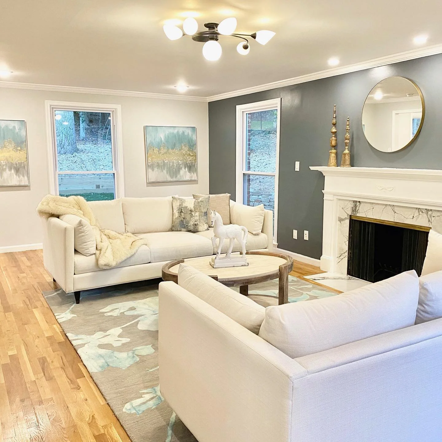 Living room with a beige sofa and loveseat, wooden coffee table, fireplace, decorative items, and windows with an outdoor view.
