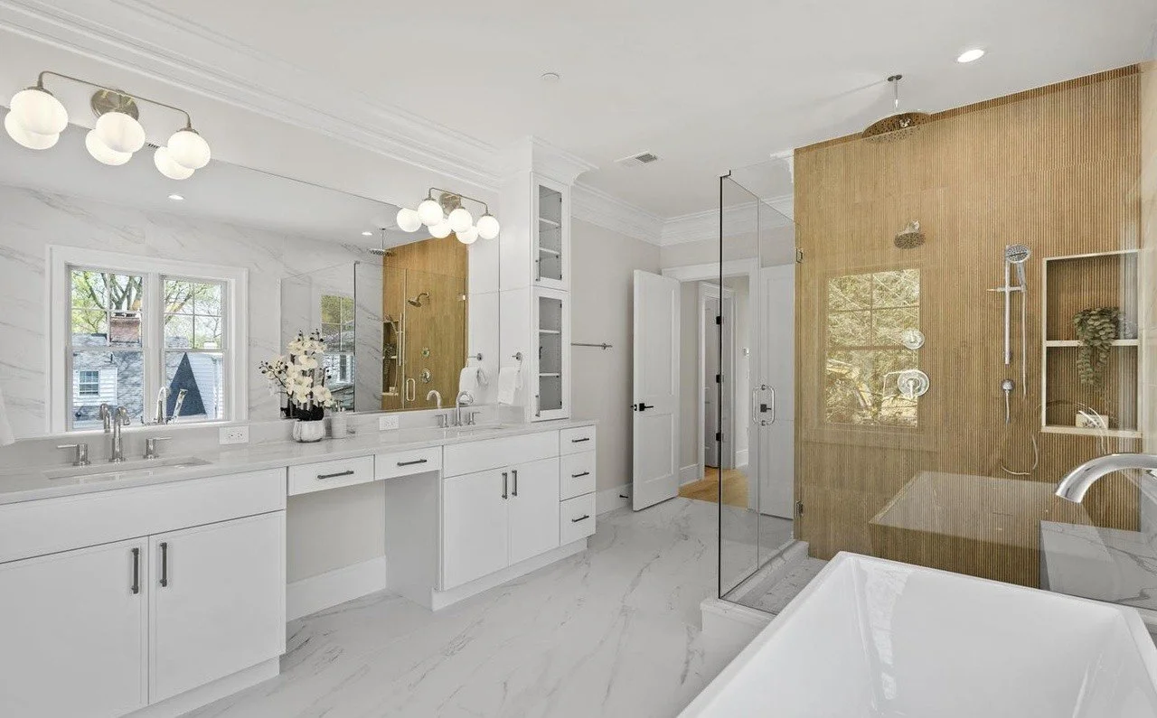 Modern bathroom with double vanity, large mirror, white cabinetry, marble countertops, and a glass enclosed shower with wooden wall accents.