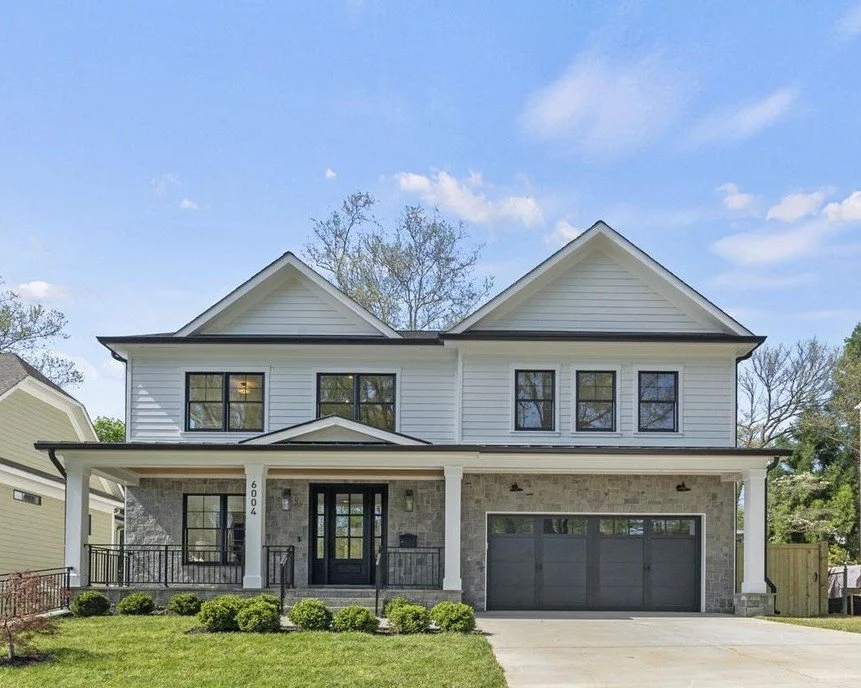 New two-story white house with black accents, stone facade, attached garage, and front yard.