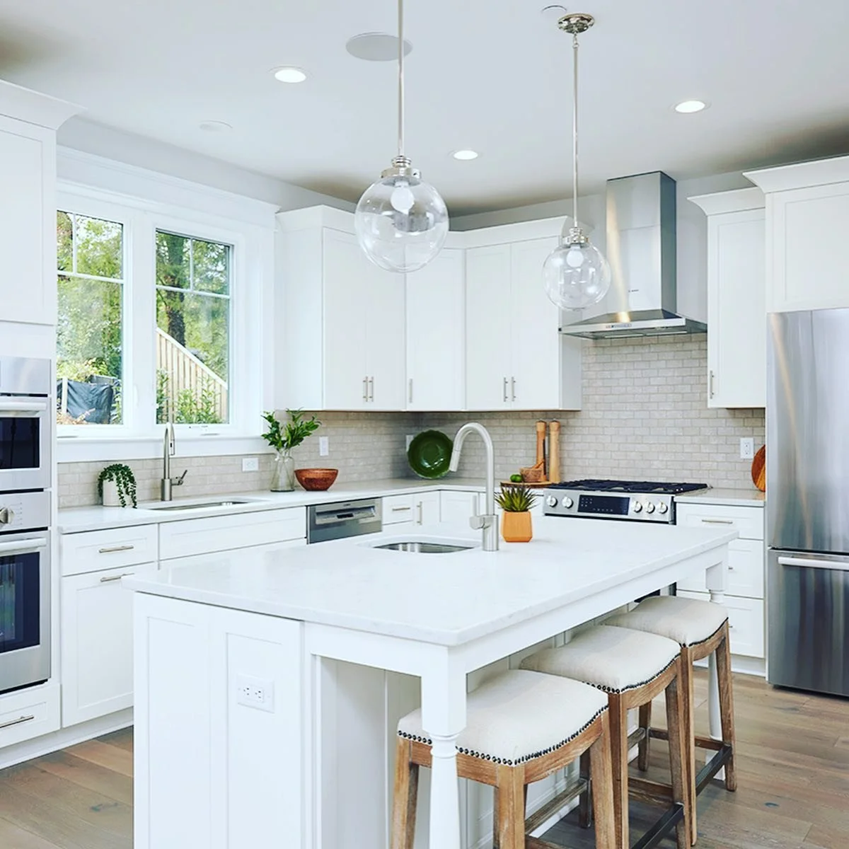 Modern white kitchen with large island, pendant lights, and stainless steel appliances.