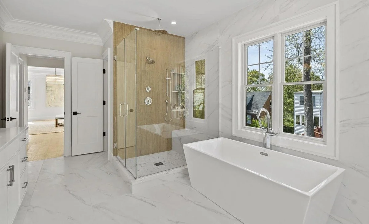 Modern bathroom featuring a white freestanding bathtub, a glass-enclosed shower with wood paneling, and a window with a view of trees outside.