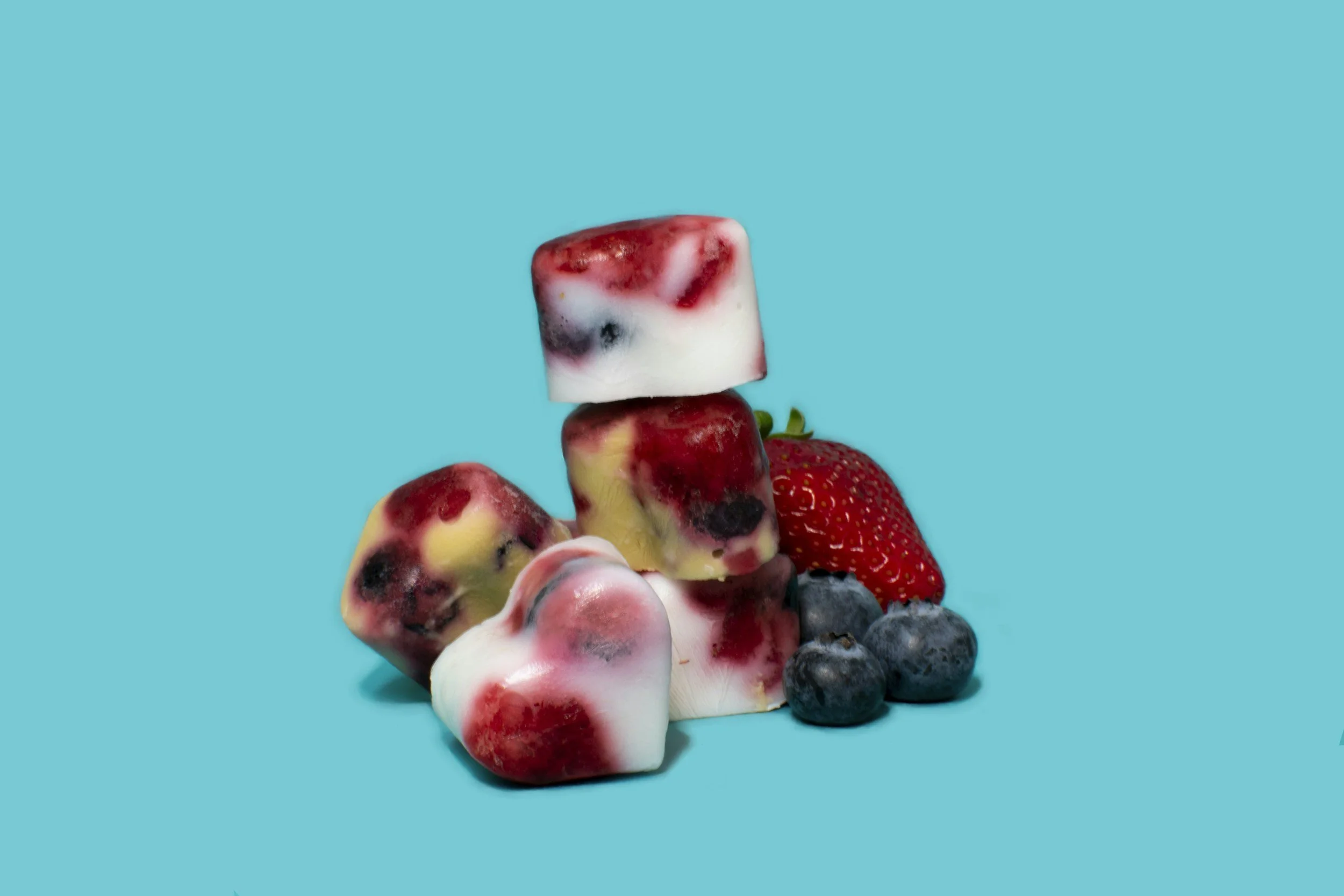A stack of heart-shaped pet treats with blueberries and a strawberry.