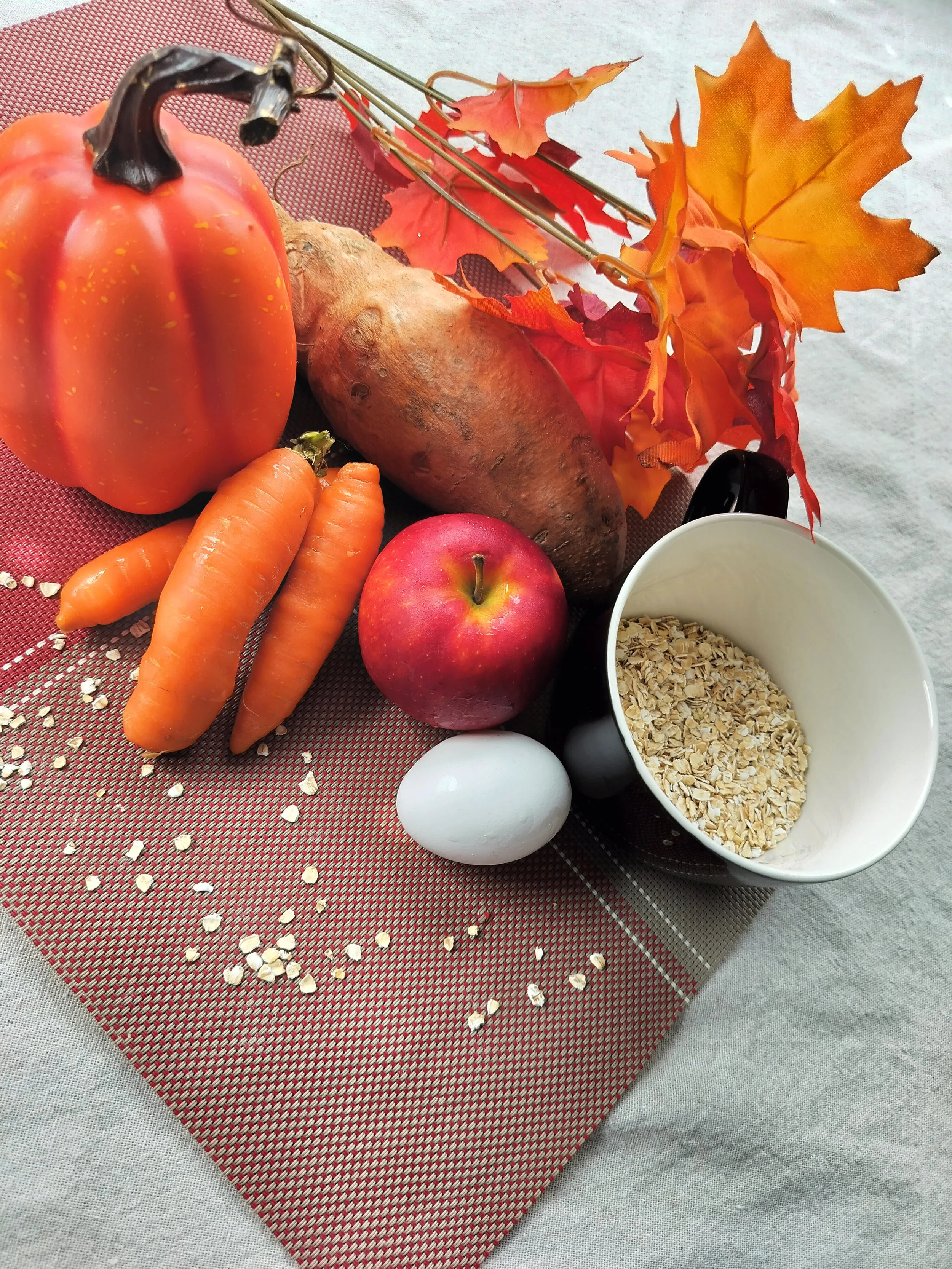 A display of dog treat ingredients including pumpkin, sweet potato, carrots, apple, rolled oats and an egg