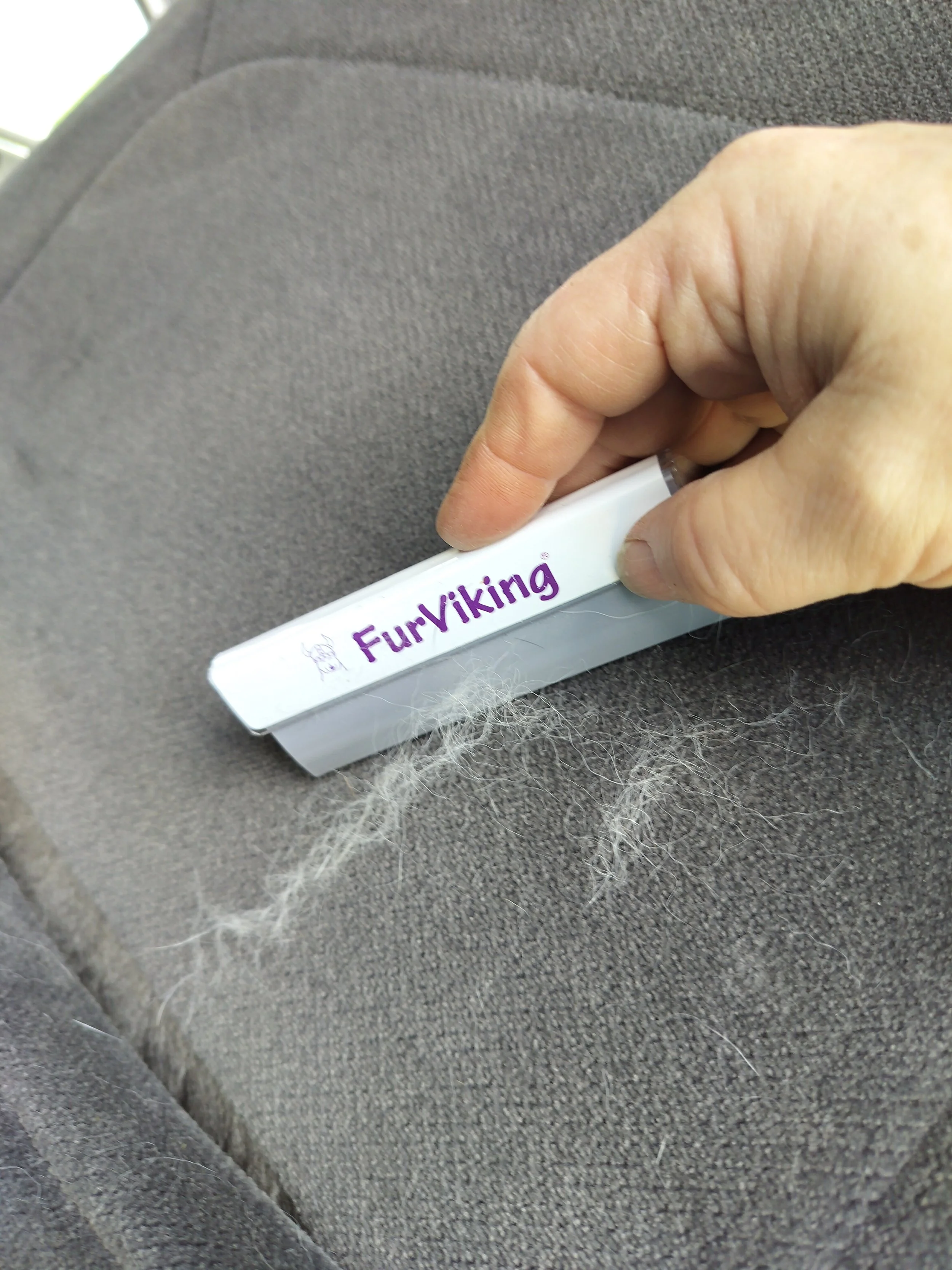 A small detailer tool being used to remove pet hair from the crevice of a car seat cushion