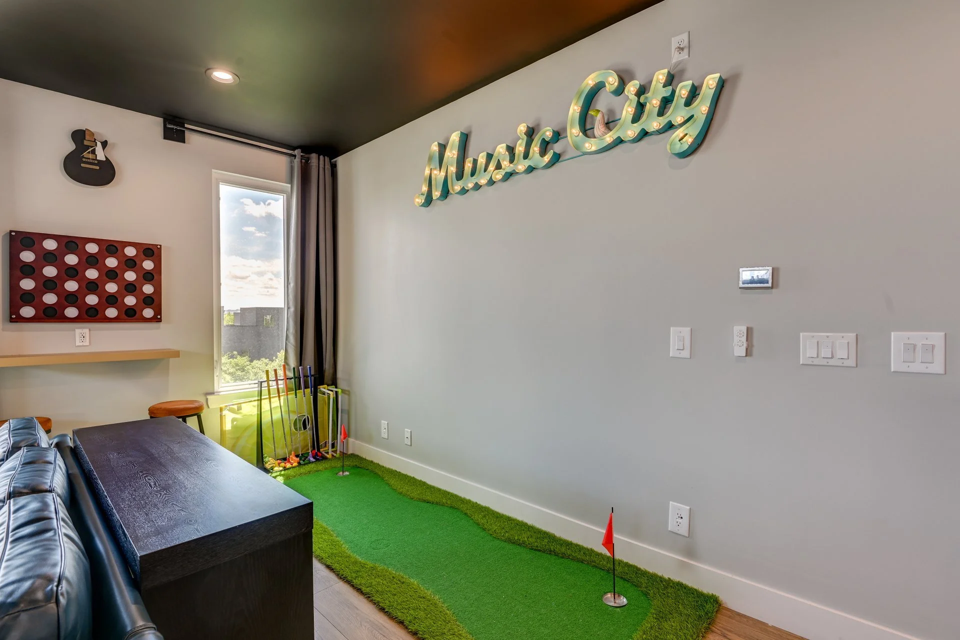 Indoor mini golf setup with a green mat, flags, and golf clubs near a window. Decor includes a guitar on the wall and a 'Music City' sign.