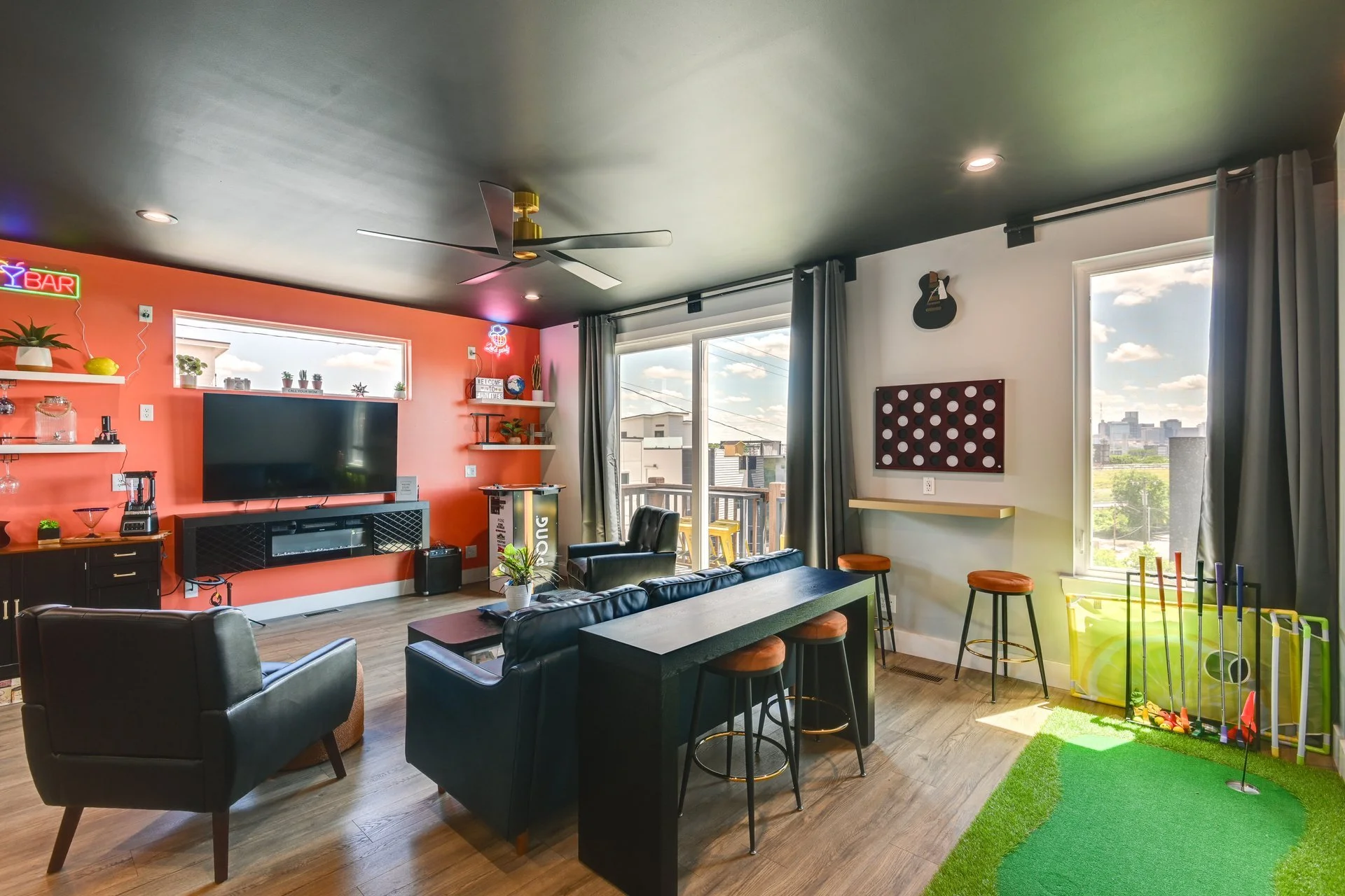 Living room with a coral accent wall, black furniture, a TV, and a balcony with a view of buildings and sky.