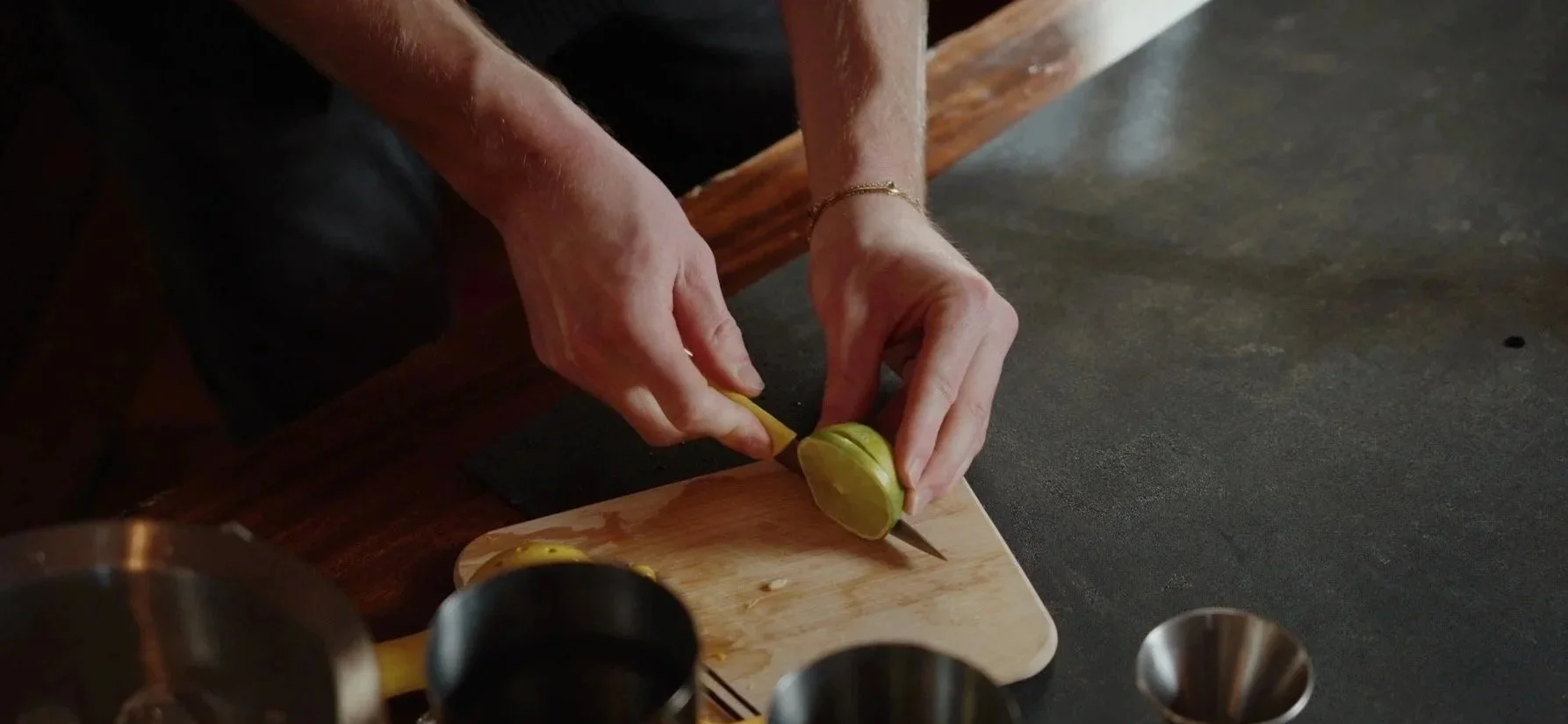 Person slicing a lemon on a wooden cutting board.