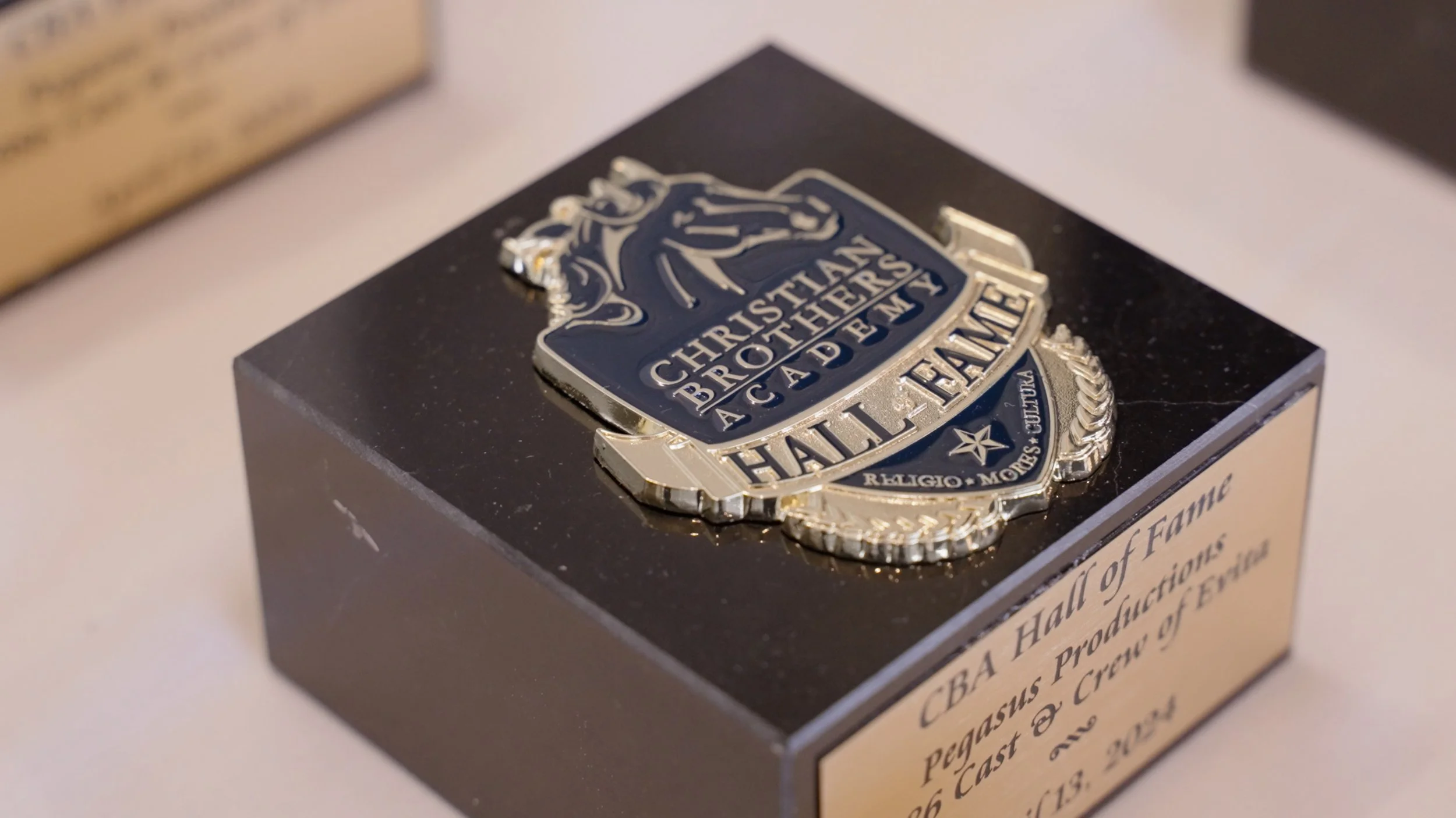 Close-up of a black display case with a shiny, silver Christian Brothers Academy Hall of Fame badge on top.
