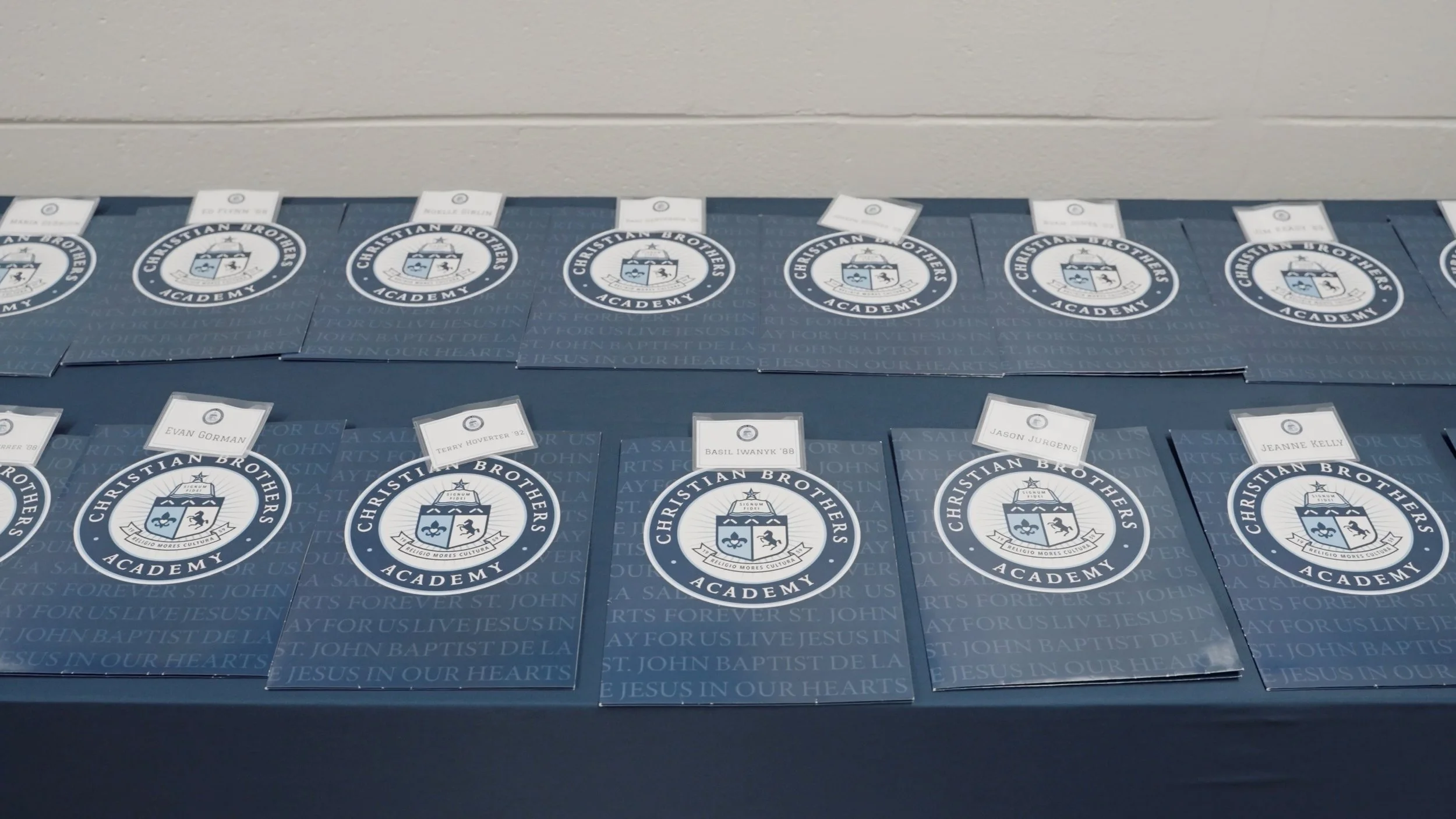 Table with Christian Brothers Academy folders and name tags, featuring school logo and motto.