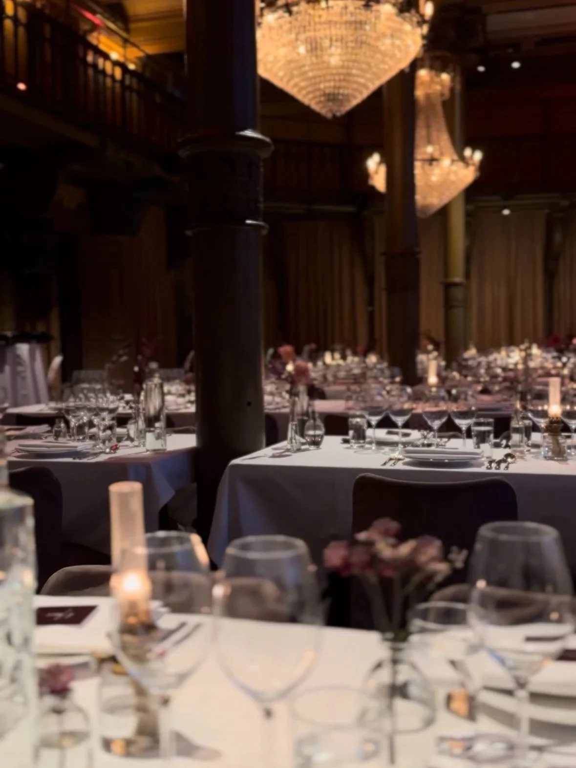 Elegant banquet hall with chandeliers, set tables with wine glasses, plates, and floral centerpieces for a formal event.