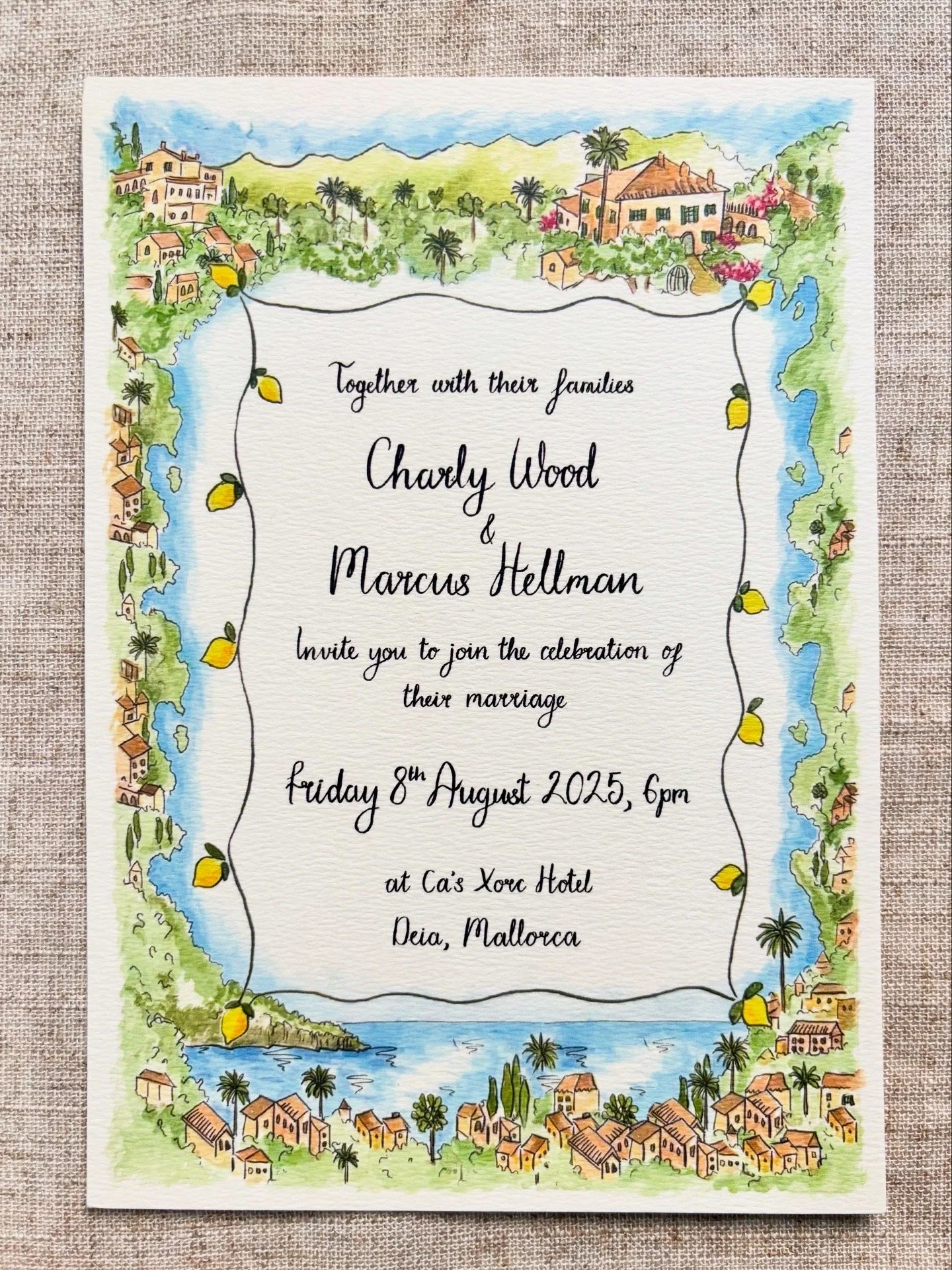 Watercolour wedding invitation with a Mediterranean village scene border, the village of Deia in Mallorca, including houses, trees, water, and hills, and yellow lemons hanging from a vine.