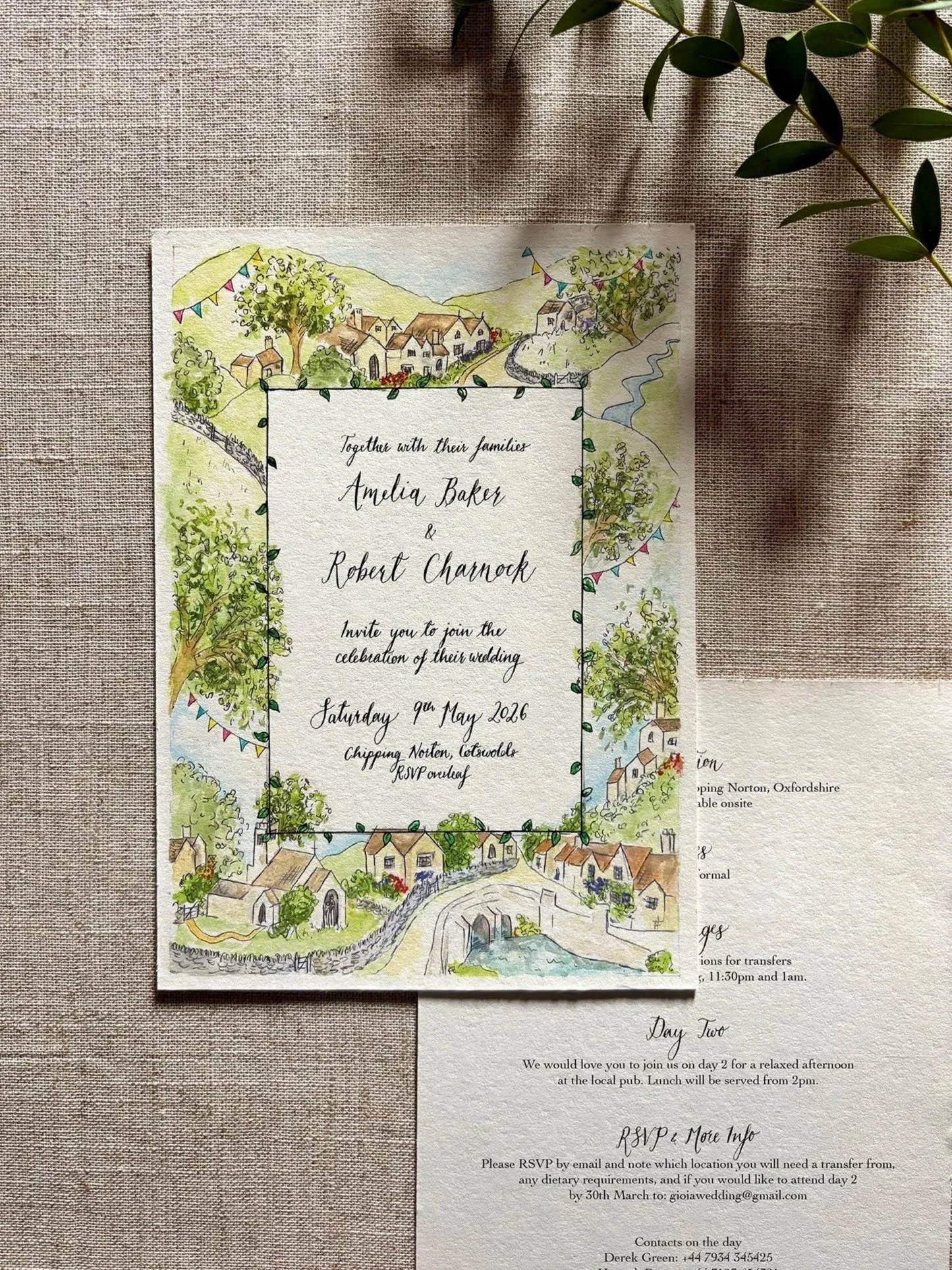 Wedding invitation with a colorful illustrated village scene border, featuring houses, trees, a river, and hills in the Cotswolds.