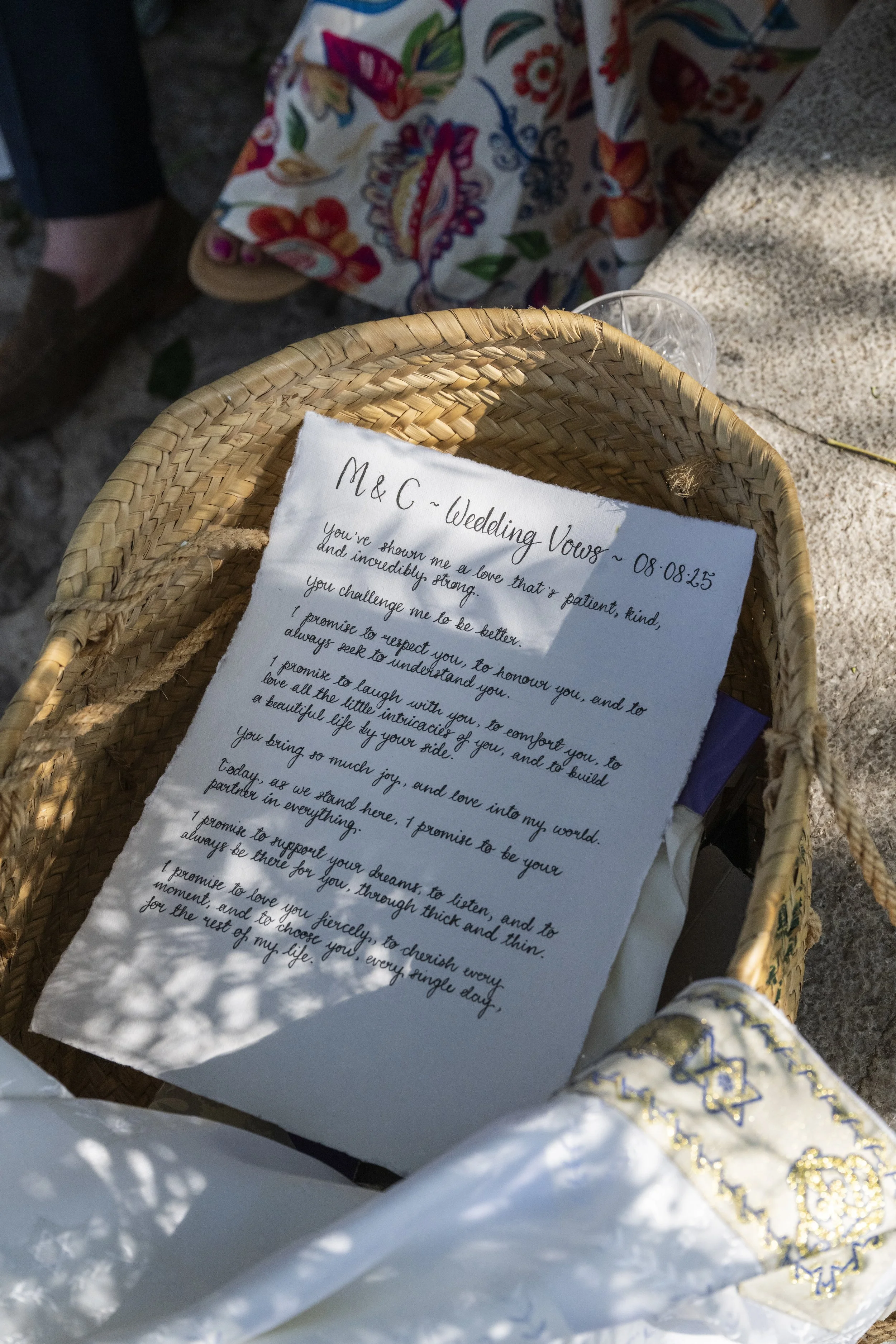 A handwritten wedding vows note inside a woven basket, with a small part of a decorated prayer shawl and other items visible nearby.