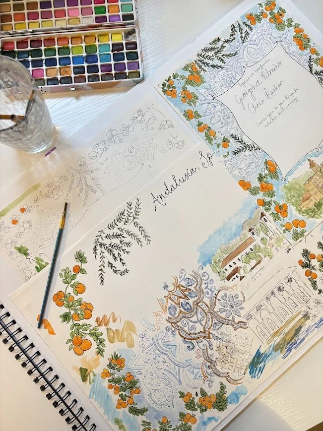 Colorful watercolor painting in progress on a sketchbook page featuring a title "Andalusia, Spain" with decorative orange and green floral borders, architectural landscape illustrations, and handwritten notes. Art supplies including watercolor paints