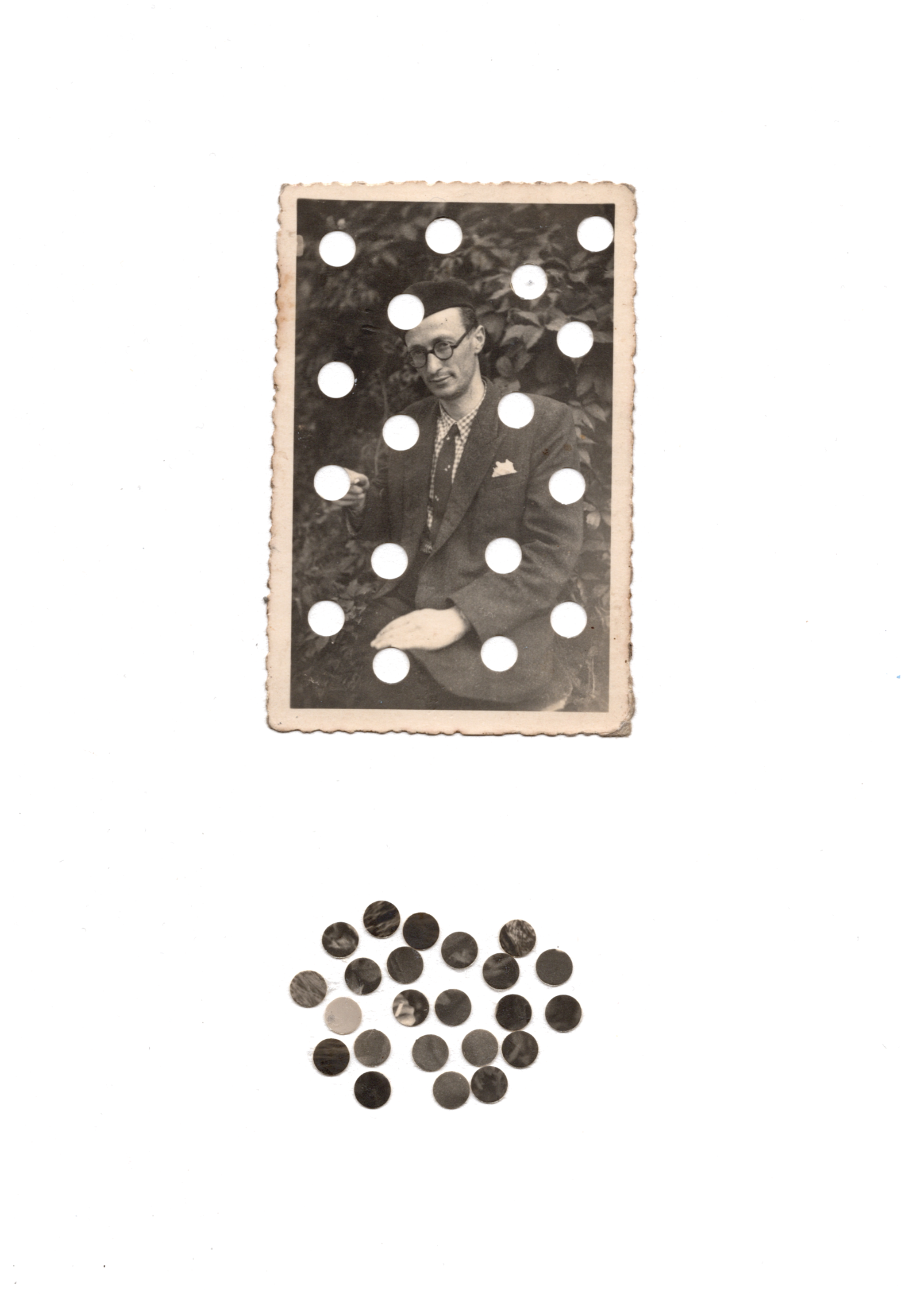 A vintage black and white photograph of a man in a suit, sitting outdoors with foliage in the background. The photo is perforated with evenly spaced circular holes. Below the photo is a small pile of black circular pebbles or buttons on a white surface.