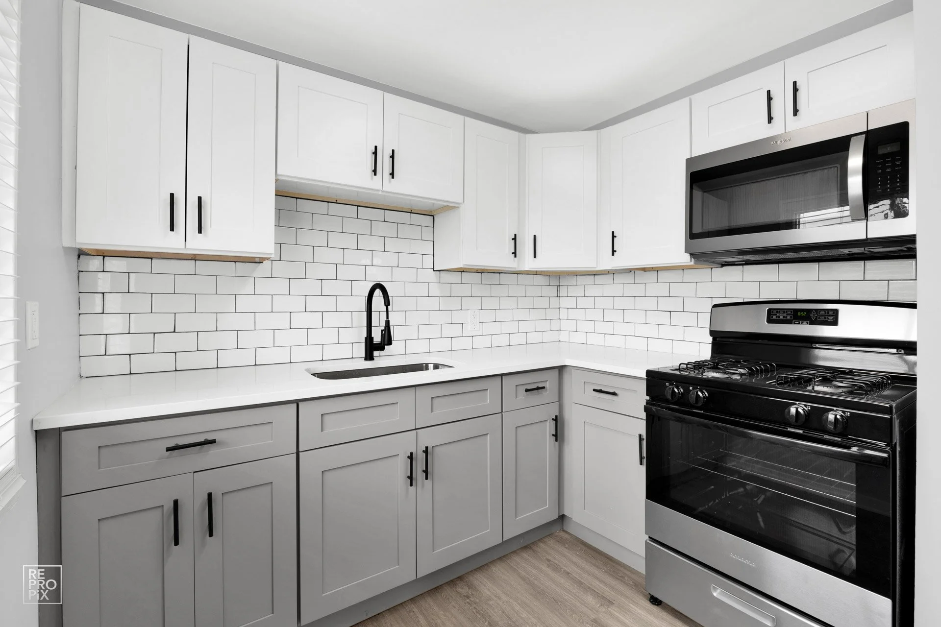 Modern kitchen with white upper cabinets, gray lower cabinets, black hardware, a white countertop, black faucet, microwave, oven, and white subway tile backsplash.