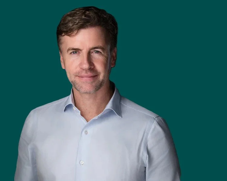 Headshot of a Andrew Marshall wearing a light blue dress shirt, smiling against a dark background.