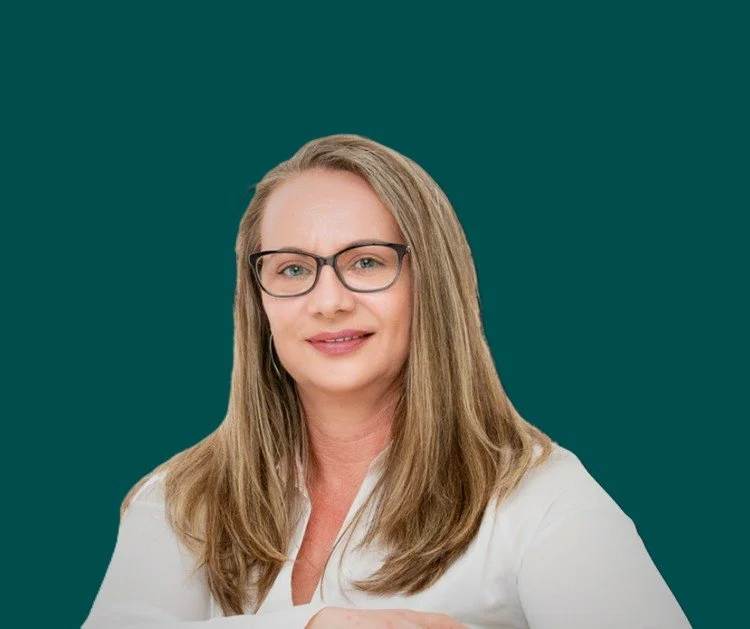 Portrait of a woman with glasses, long light brown hair, wearing a white shirt, against a dark background.