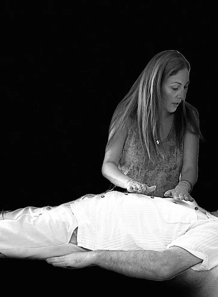 Une femme pratique une préparation ou une caresse lors d'une séance de massage ou de soins, avec un homme allongé sur une table. Illustration en noir et blanc.