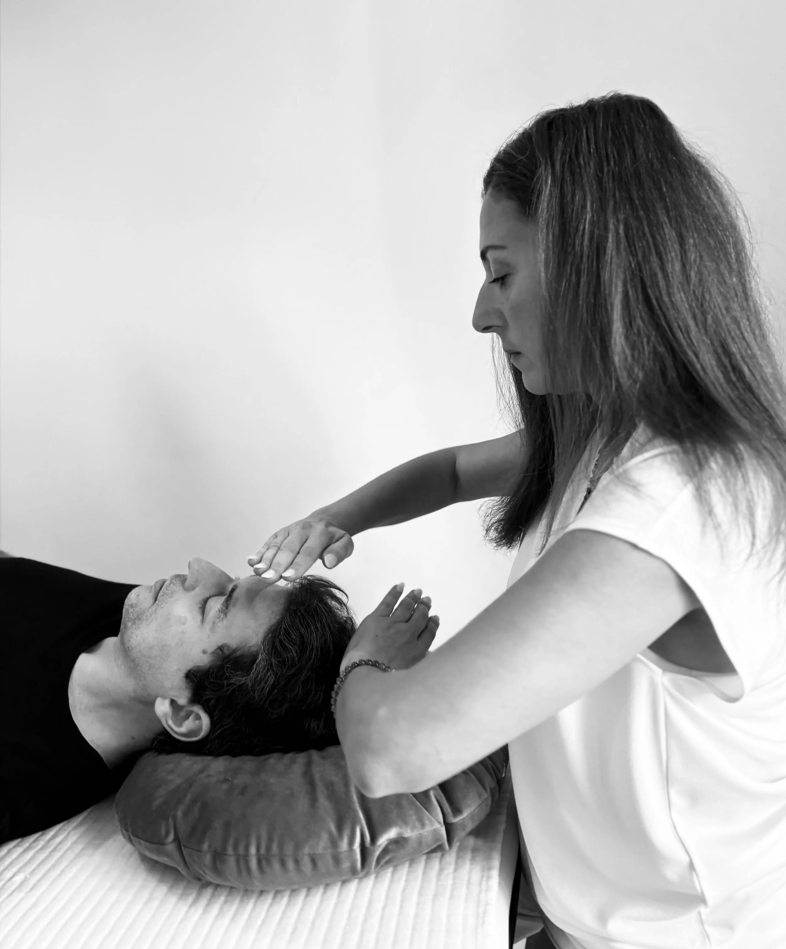 Une femme pratiquant une séance de reiki à un homme allongé, posant ses mains au-dessus de son visage dans une pièce blanche