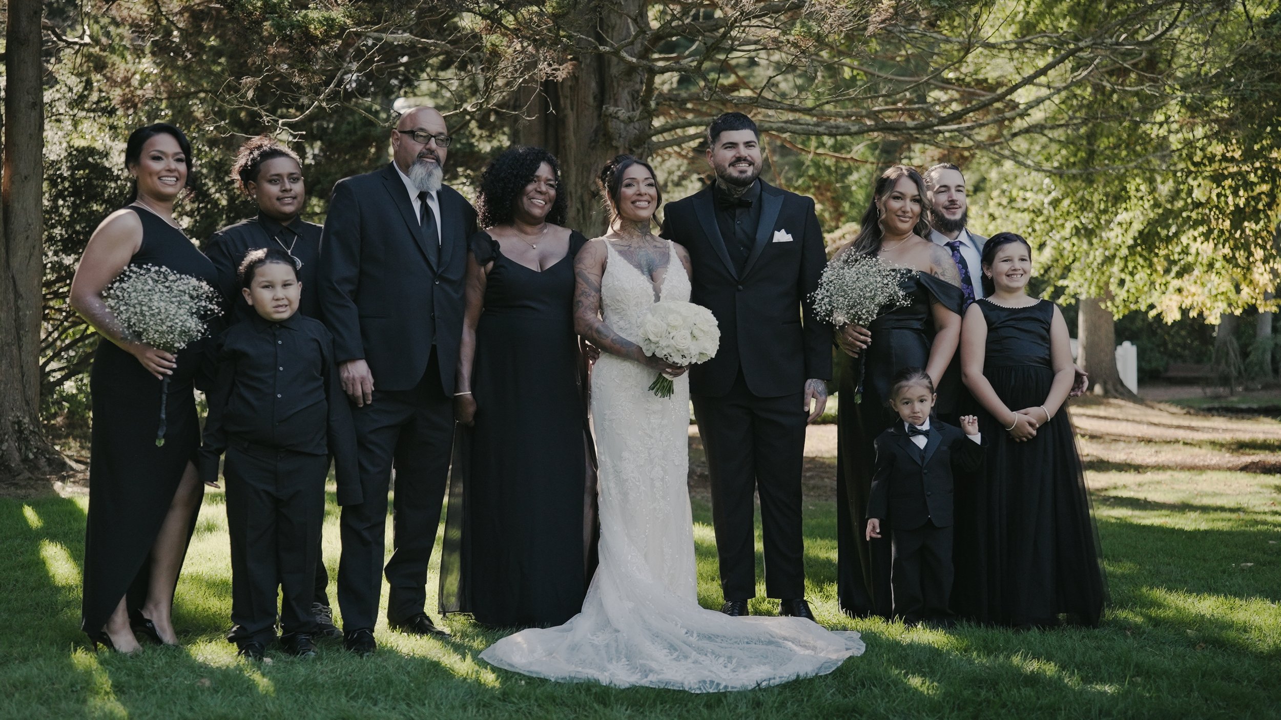 A group of women dressed in blue and one in a wedding dress with a sunflower crown, holding bouquets, standing outdoors in a wooded area during a celebration or ceremony.