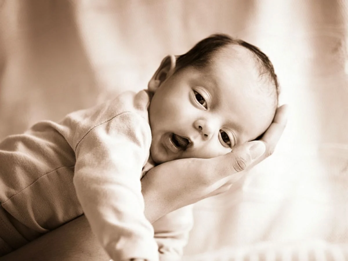 A baby with a serious expression being gently cradled in an adult's hand.