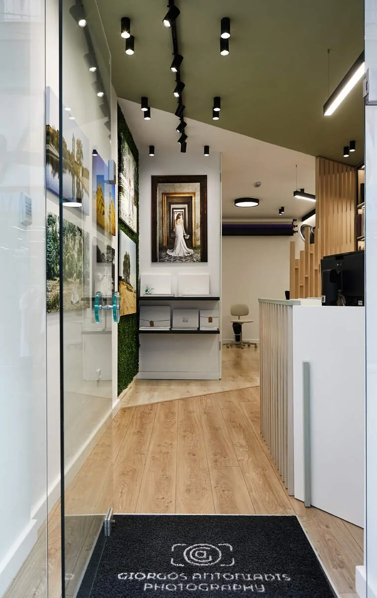 Interior of a photography studio with artwork on the walls, a black ceiling with track lighting, and a reception area with a computer and seating.